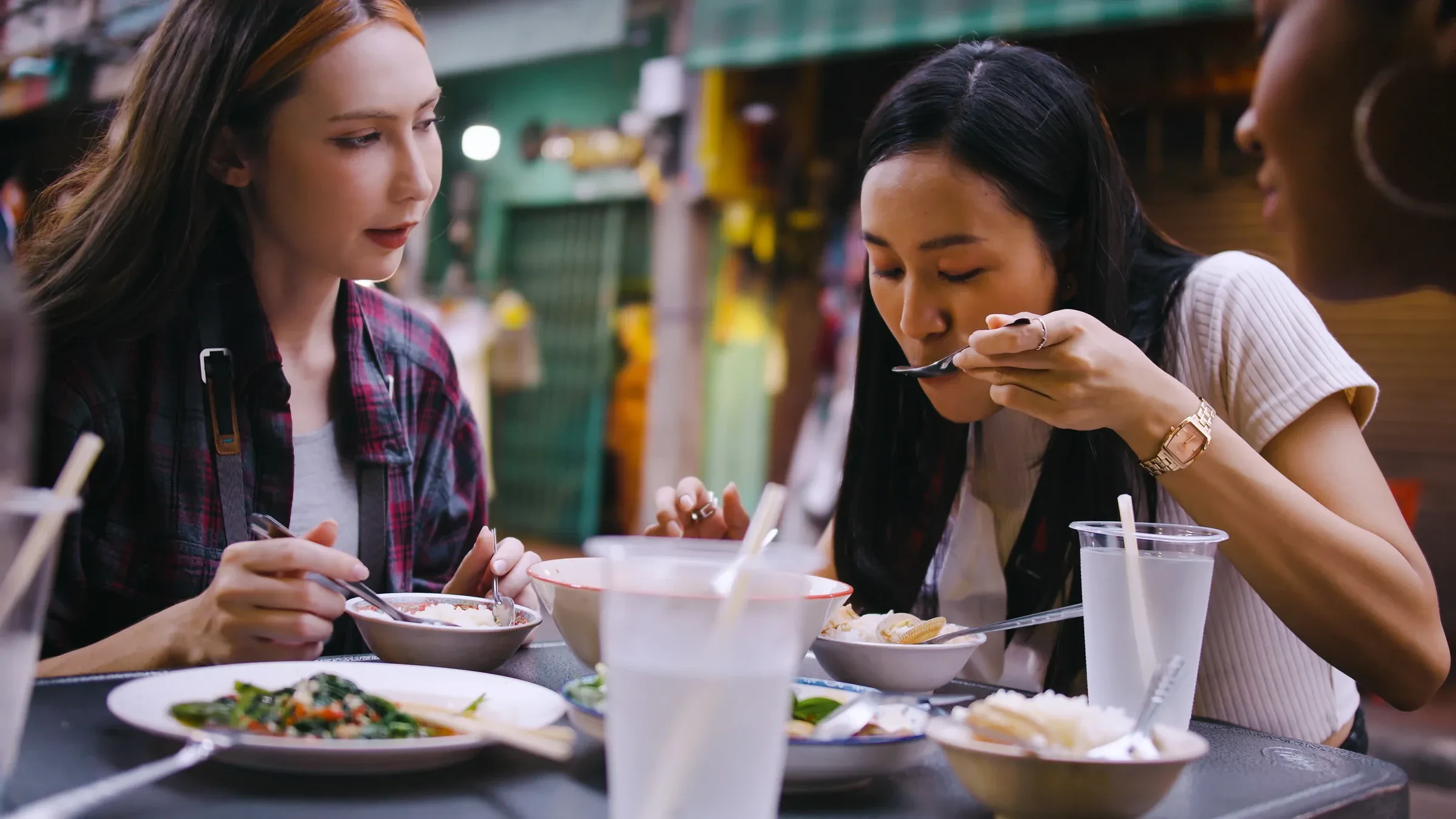 Two friends sharing plates at a street food stall in Bangkok