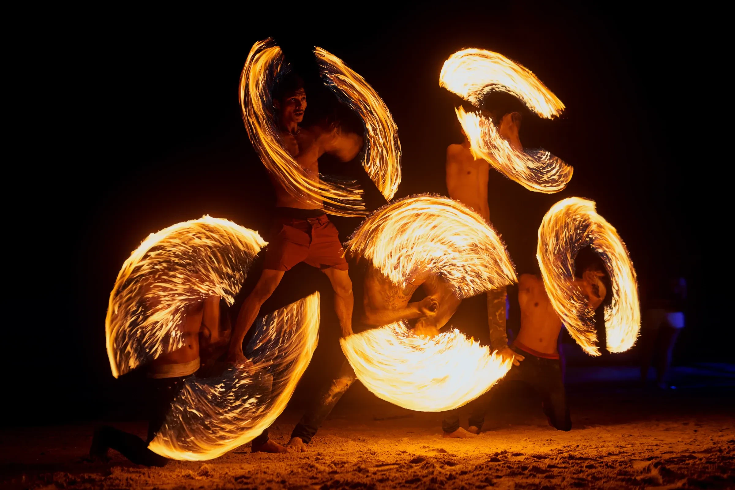 Fire dancers twirling flaming hoops on a beach at night