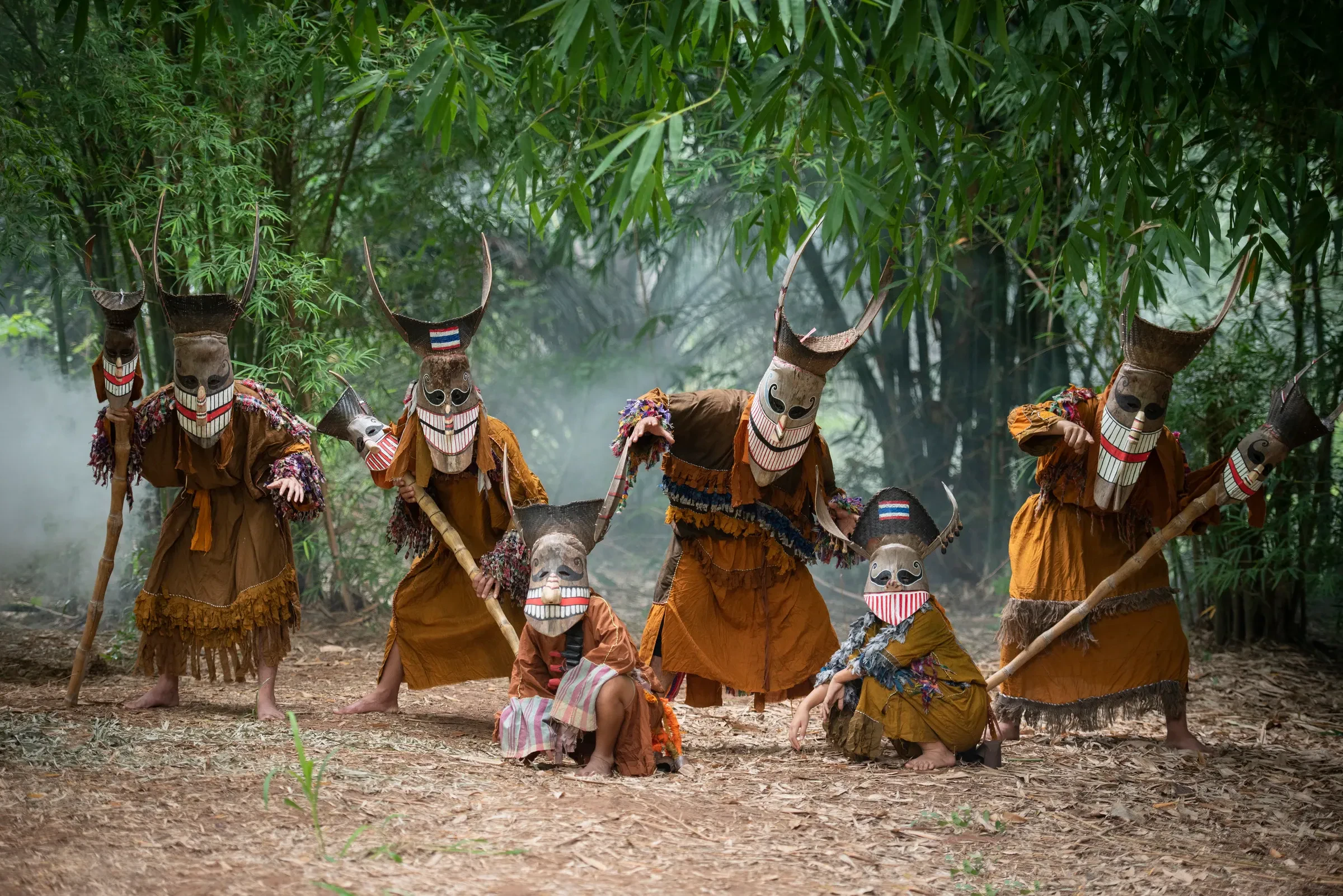 People in Phi Ta Khon ghost costumes and coconut-husk masks holding staffs in a bamboo grove in Dan Sai