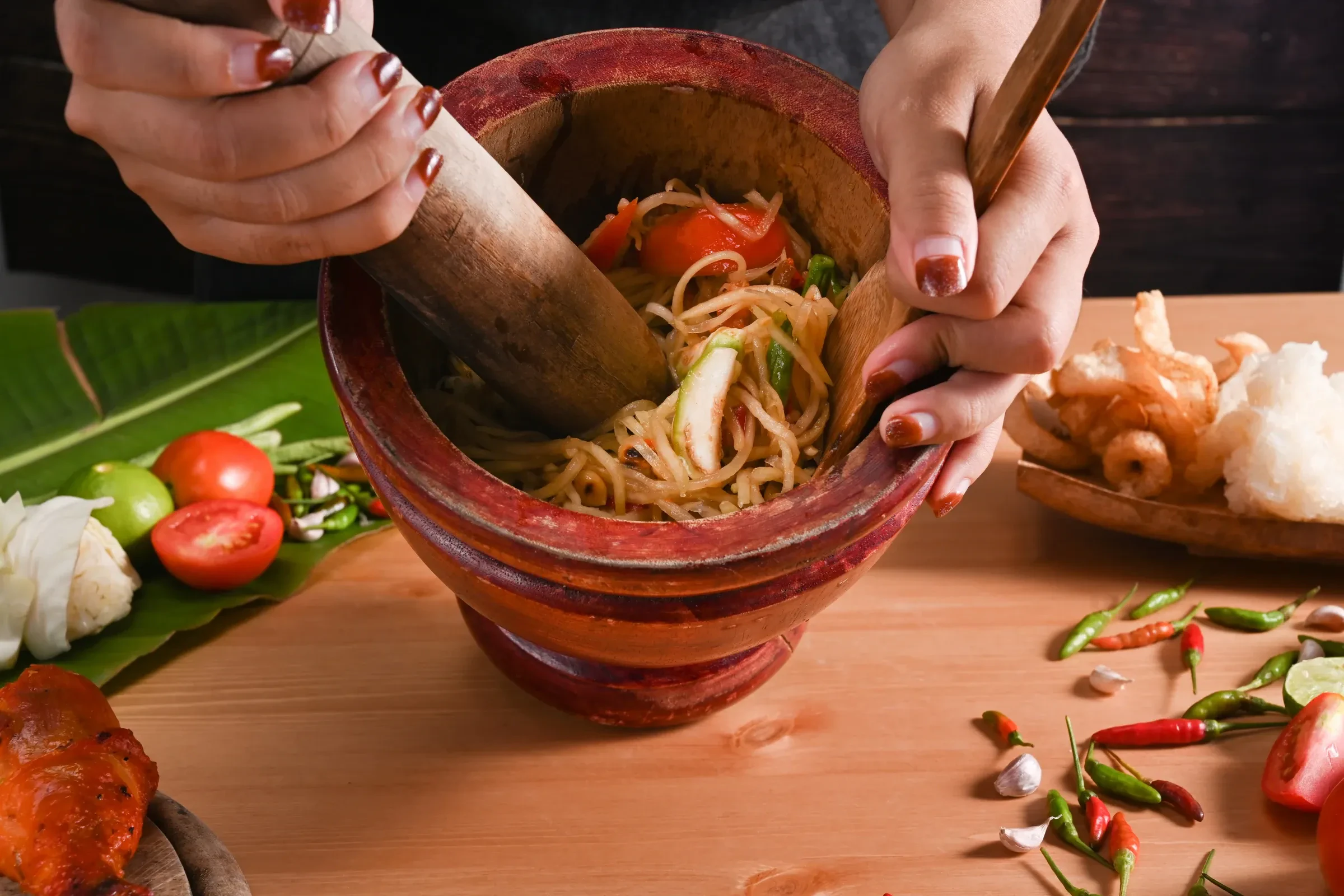 Hands pounding som tam, green papaya salad, in a clay mortar