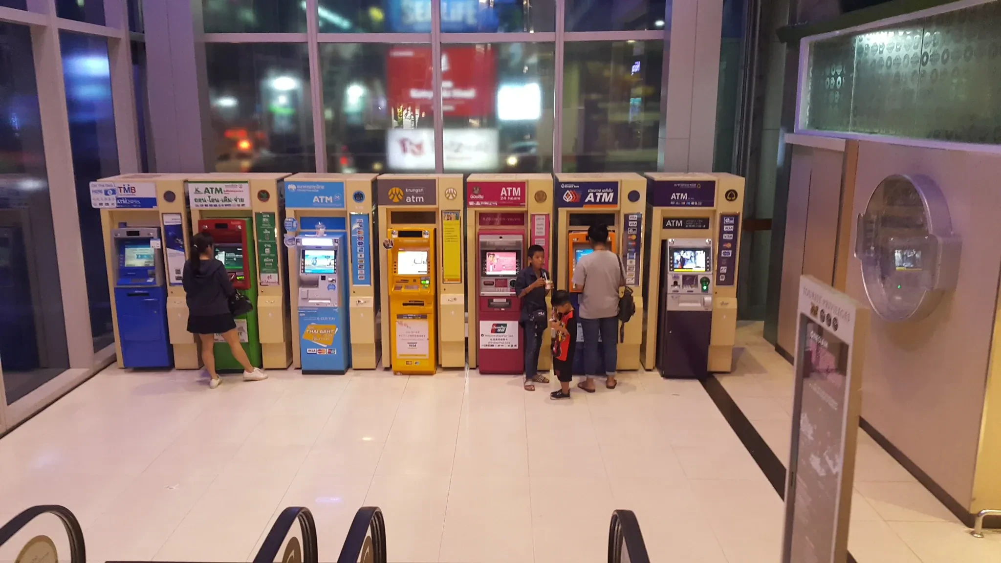 People using a row of bank ATMs in a Bangkok shopping centre