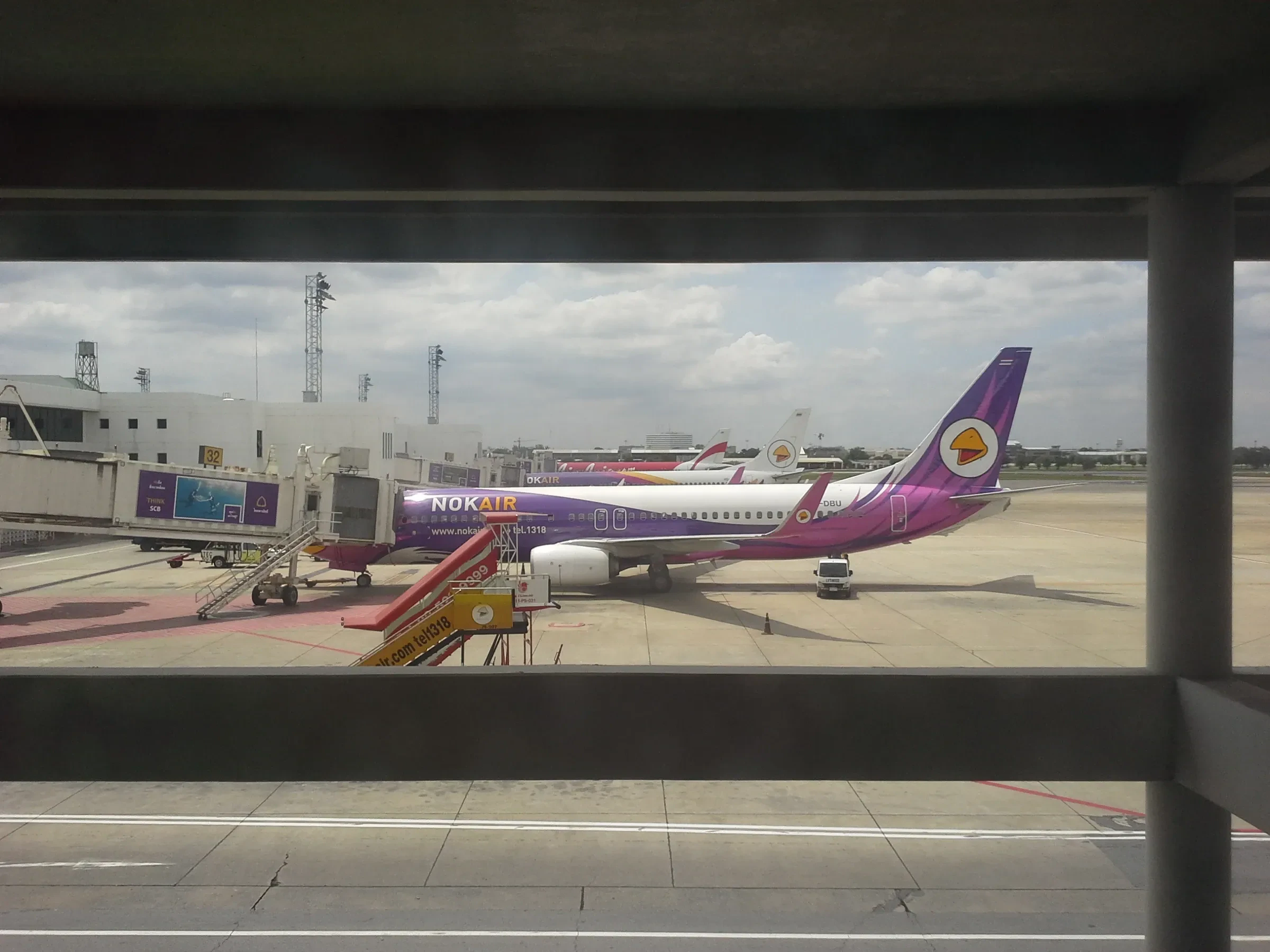 A Nok Air plane at a gate at Don Mueang Airport, seen through a terminal window