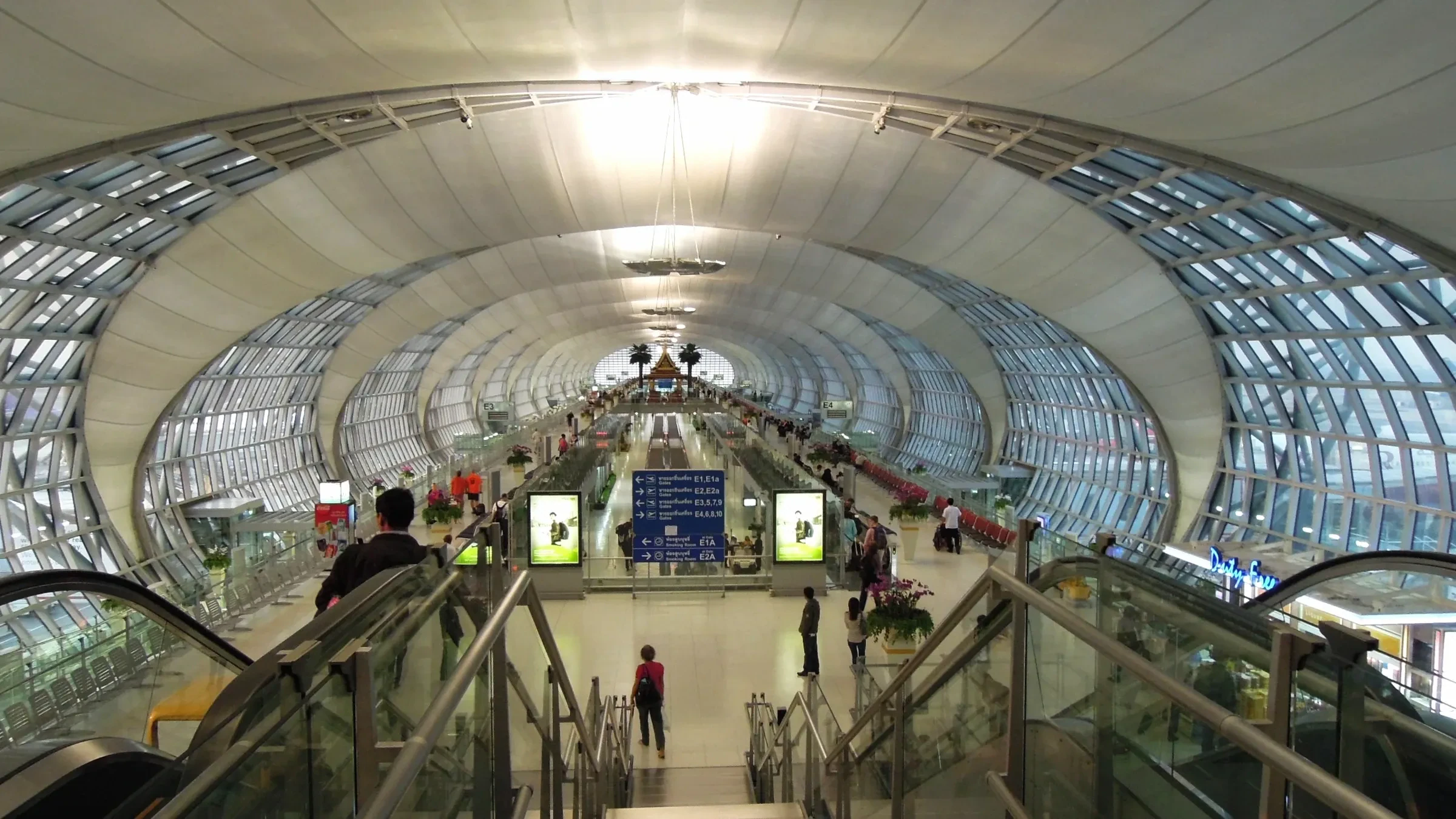 A long concourse under a curved glass roof inside Suvarnabhumi Airport in Bangkok