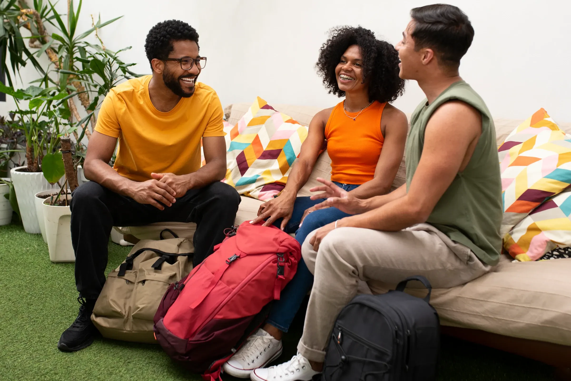 Three travellers with backpacks chatting on a sofa in a hostel lounge