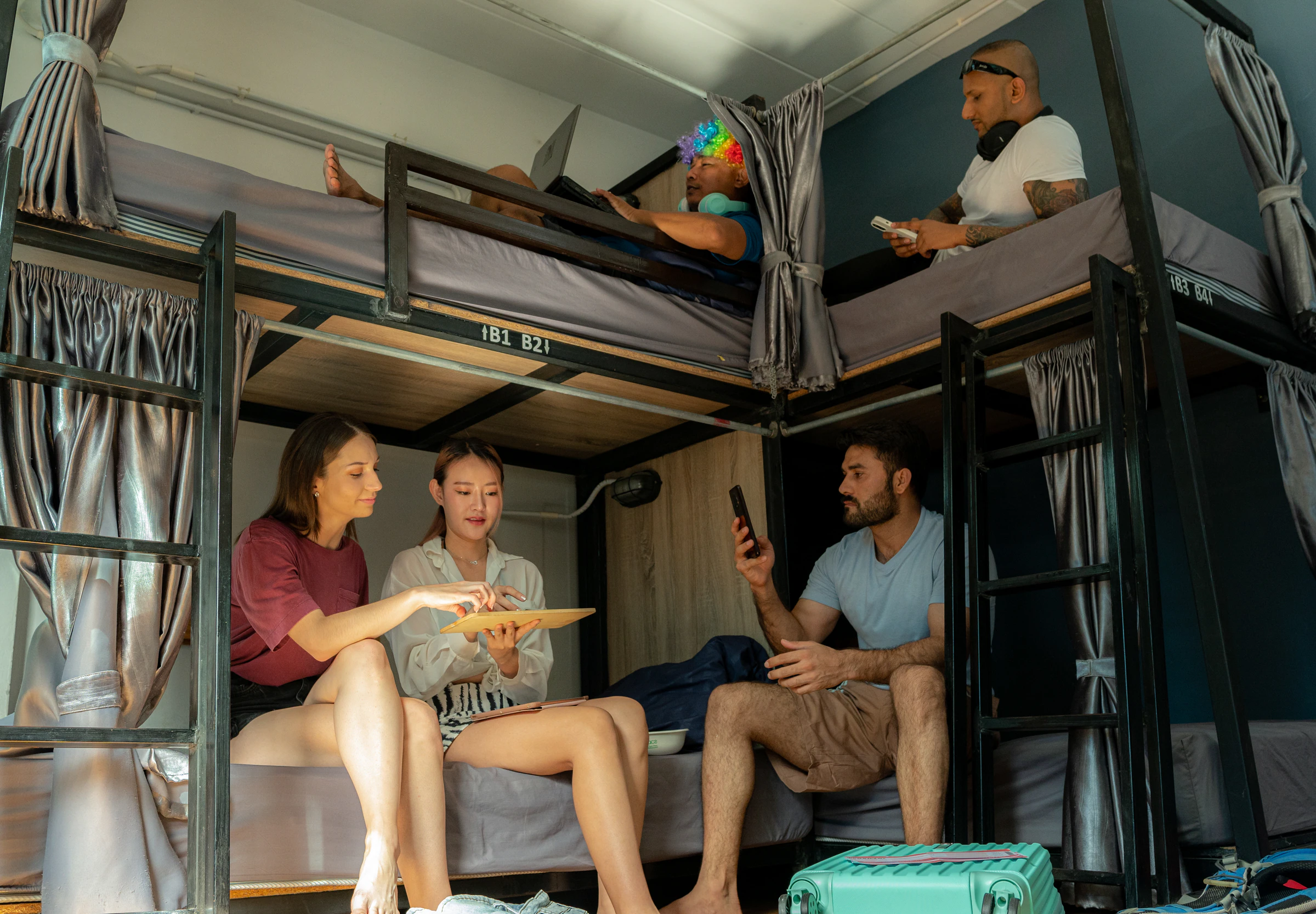 Travellers chatting and planning around the bunk beds of a hostel dorm