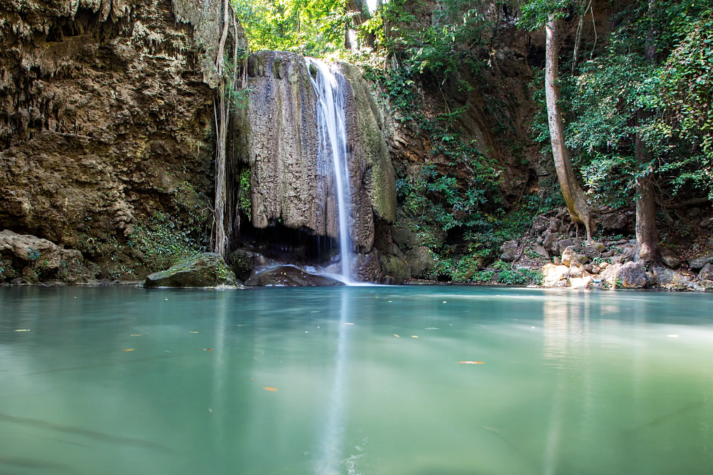 A waterfall dropping into a turquoise pool in the forest at Erawan National Park