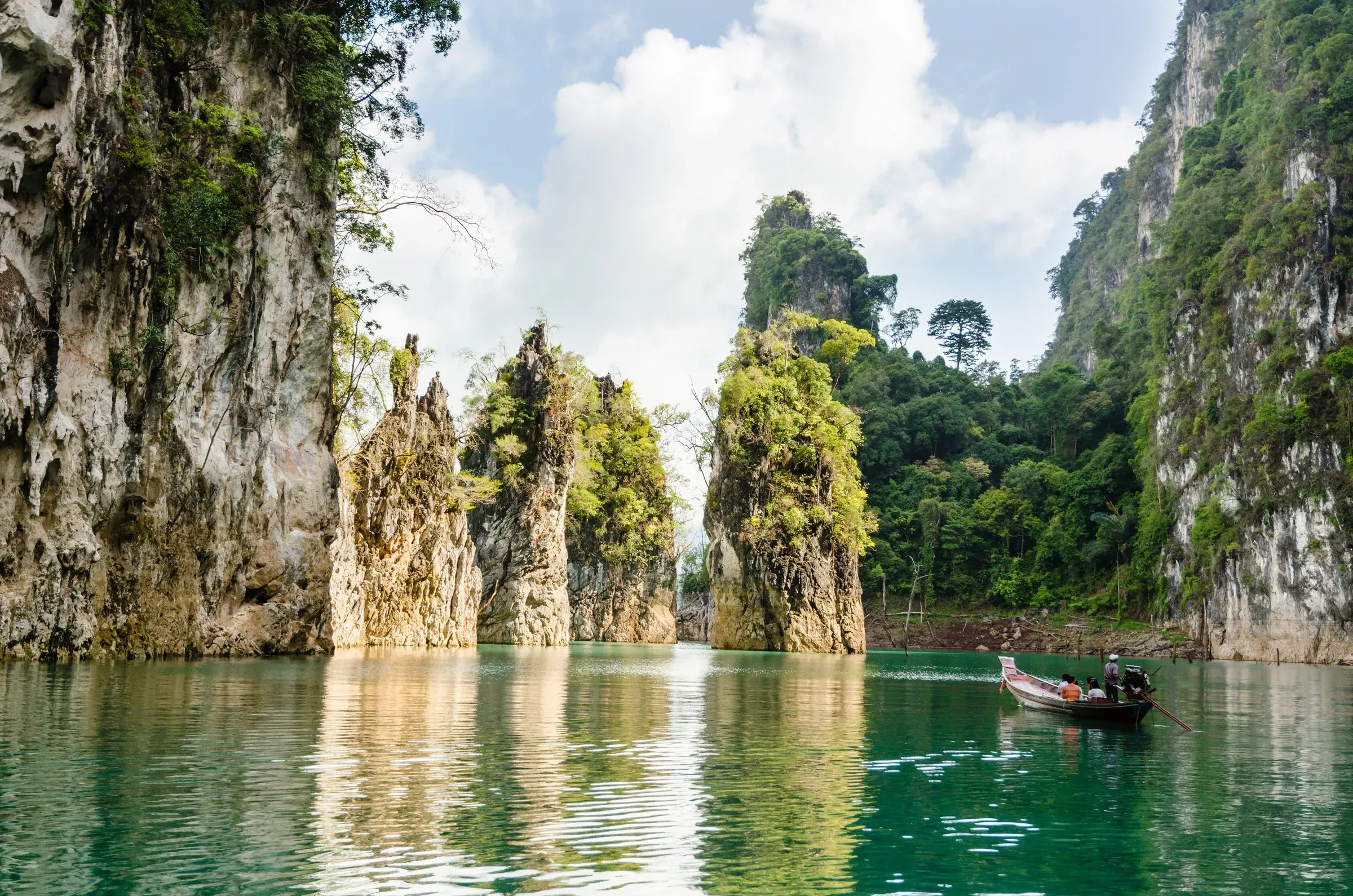 A longtail boat passing limestone towers on a green lake in Khao Sok