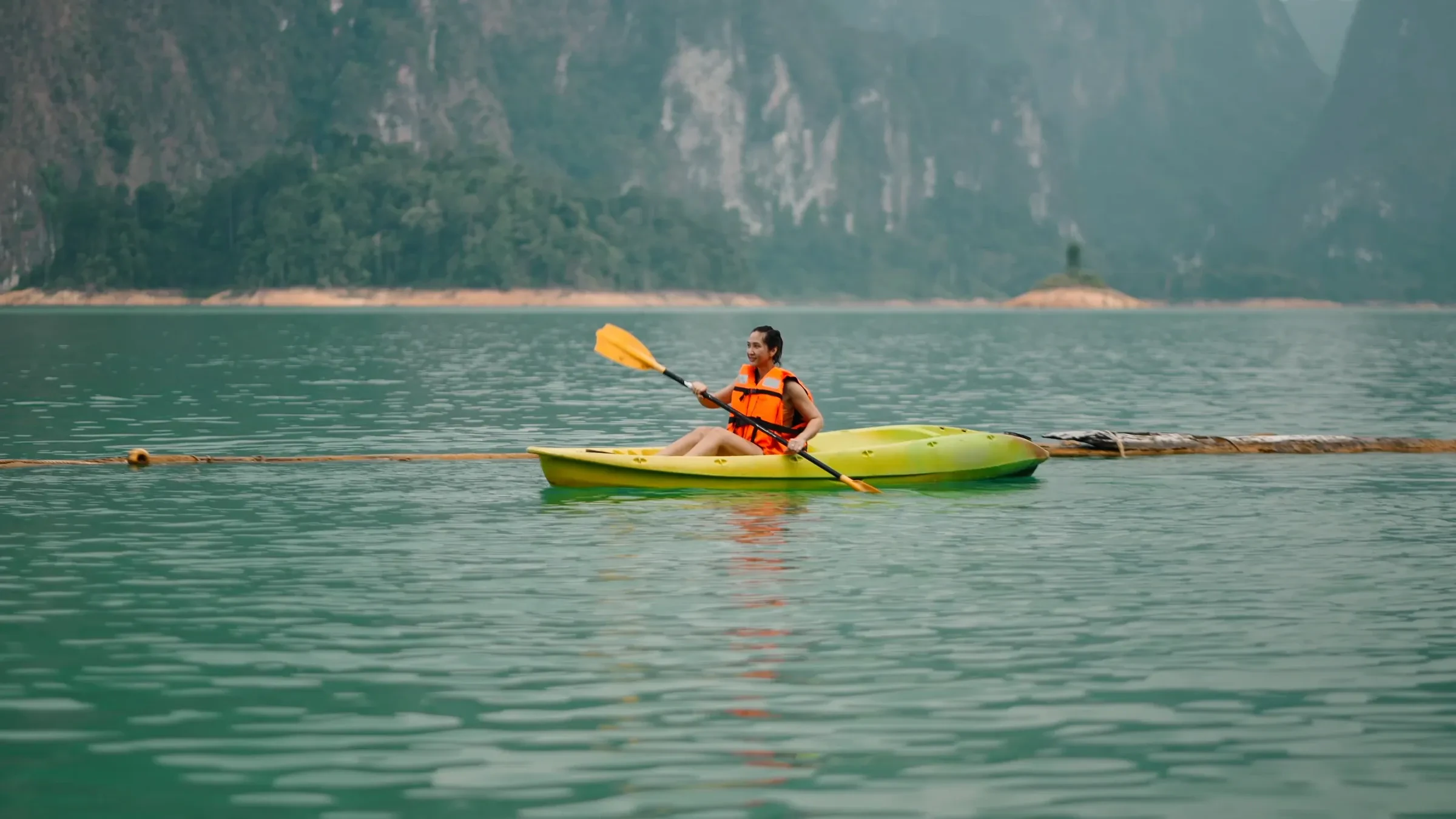 A kayaker paddling across a Khao Sok lake below forested karst hills
