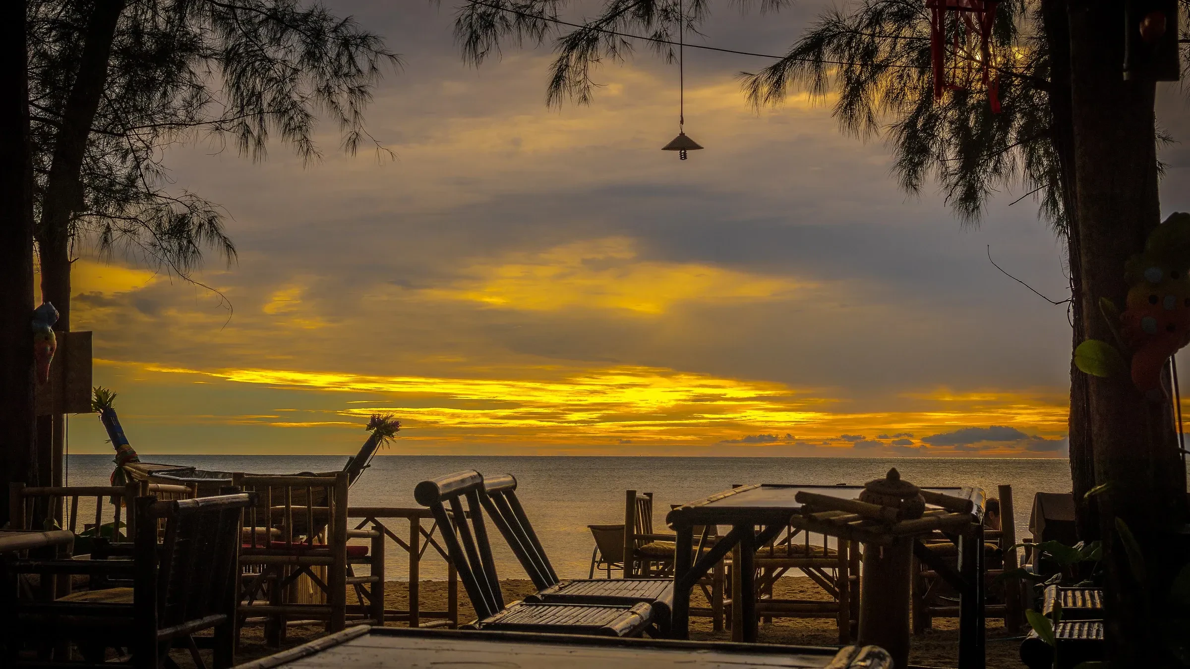 Bamboo tables at a beach bar on Koh Lanta under a golden sunset sky