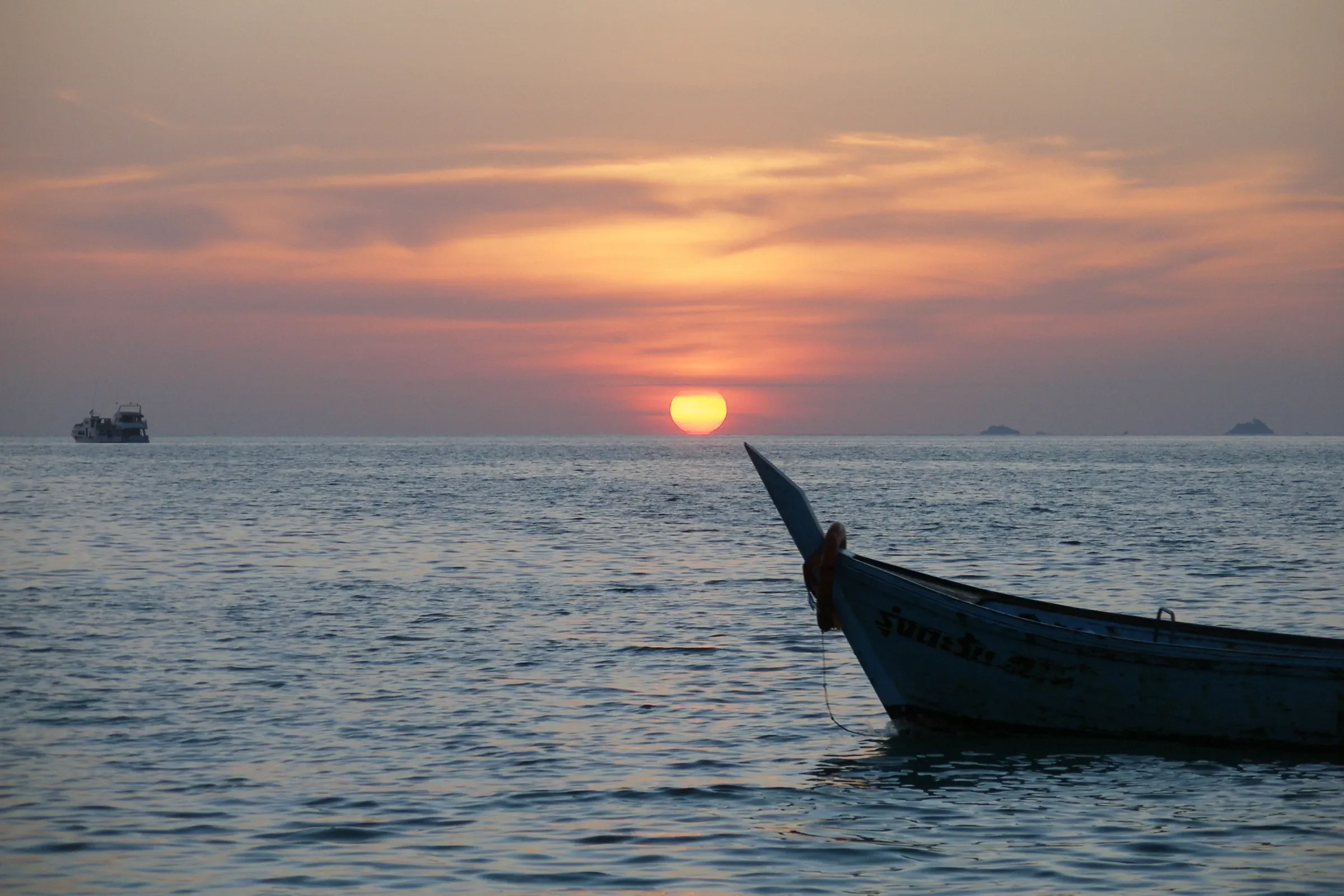 The sun setting over the sea behind a longtail boat bow, off Koh Lipe