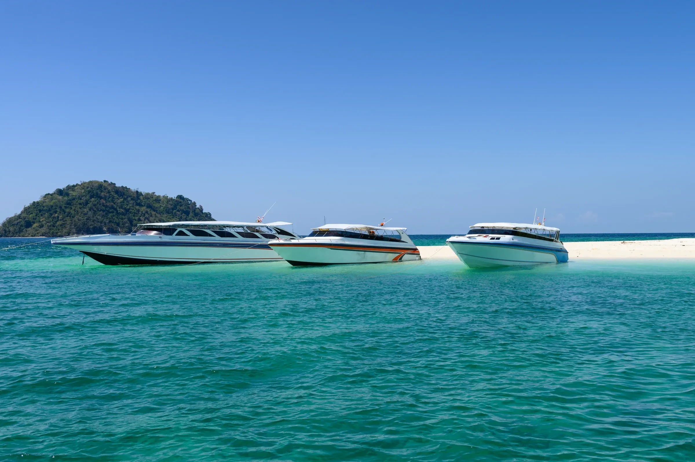 Speedboats anchored off a white sand beach in clear turquoise water
