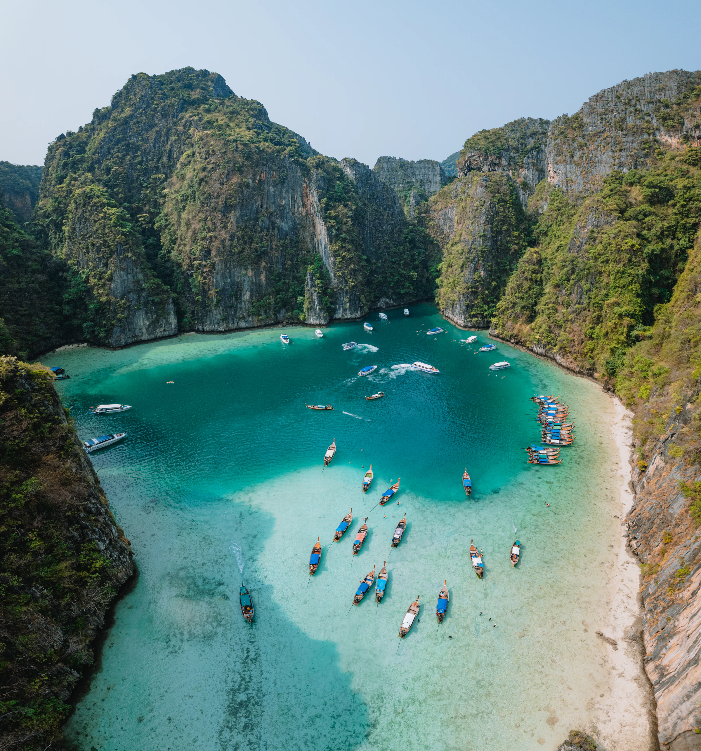 Aerial view of longtail boats in a turquoise cove ringed by limestone cliffs in the Phi Phi islands