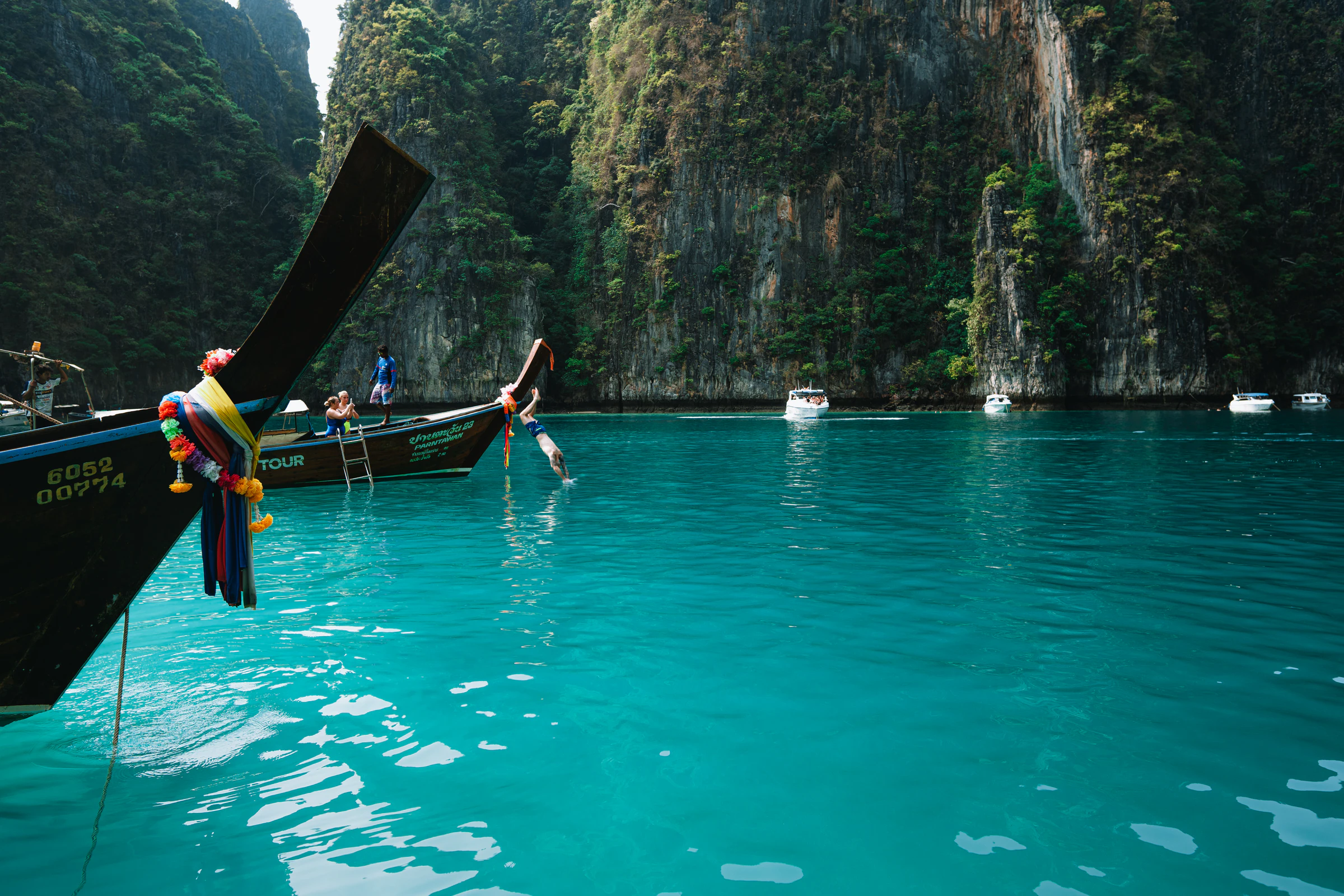 A swimmer jumping from a longtail boat into turquoise water below limestone cliffs in the Phi Phi islands