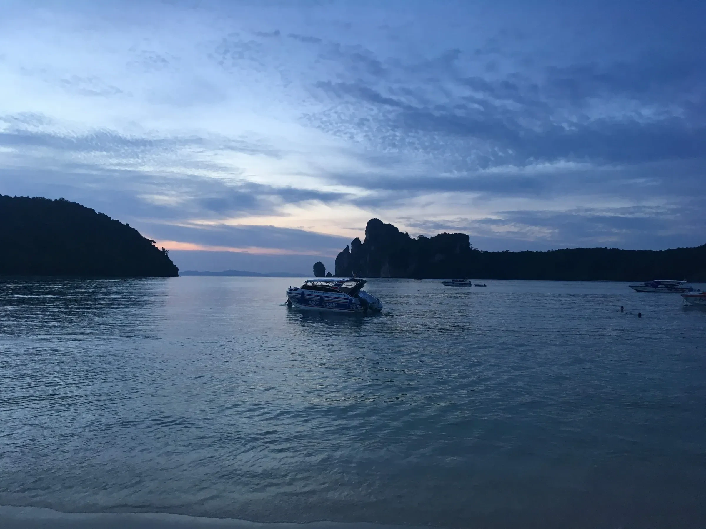 Dusk over Loh Dalum Bay on Koh Phi Phi Don, with a speedboat and limestone headlands
