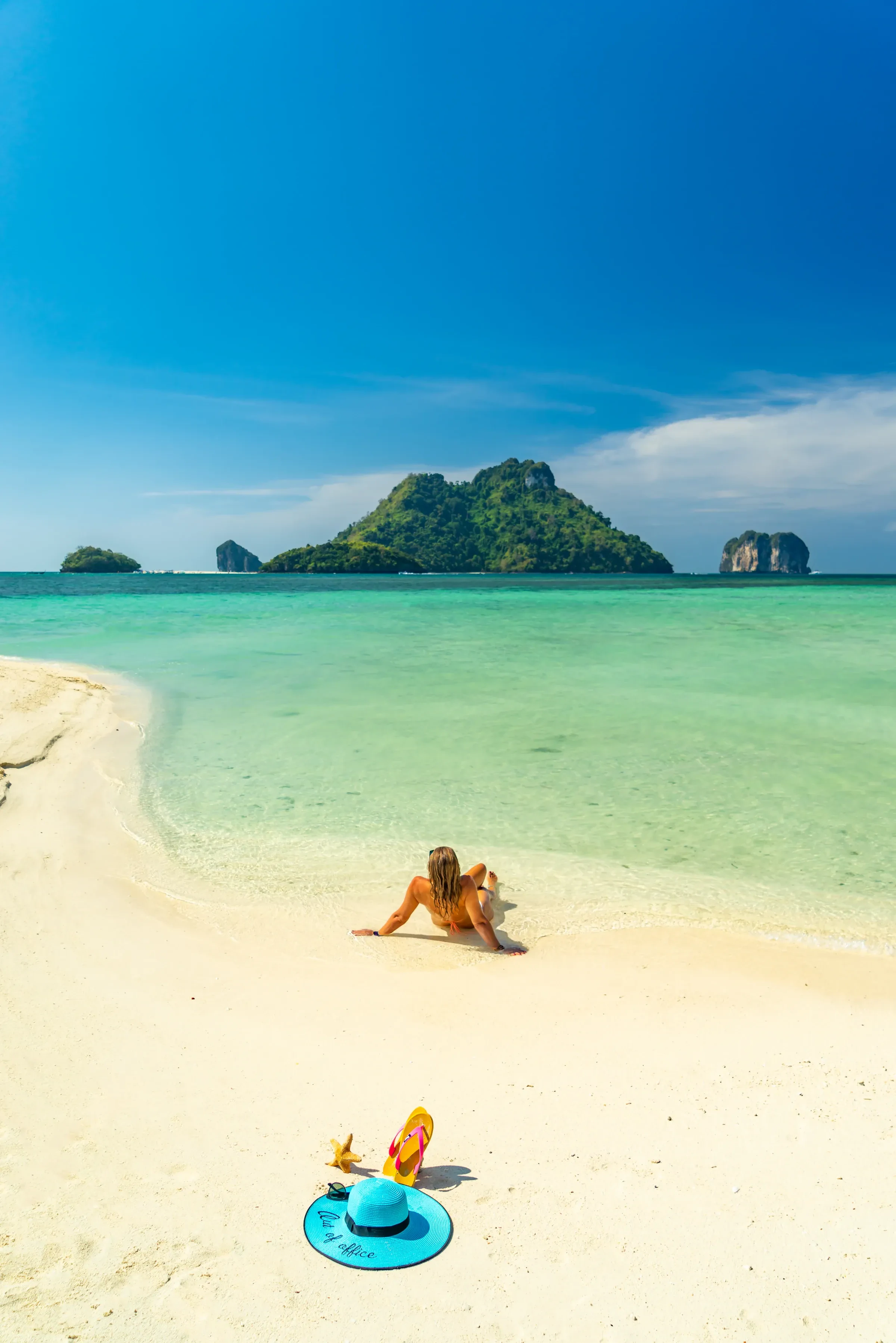 A traveller on a Krabi beach with turquoise water and a limestone island offshore