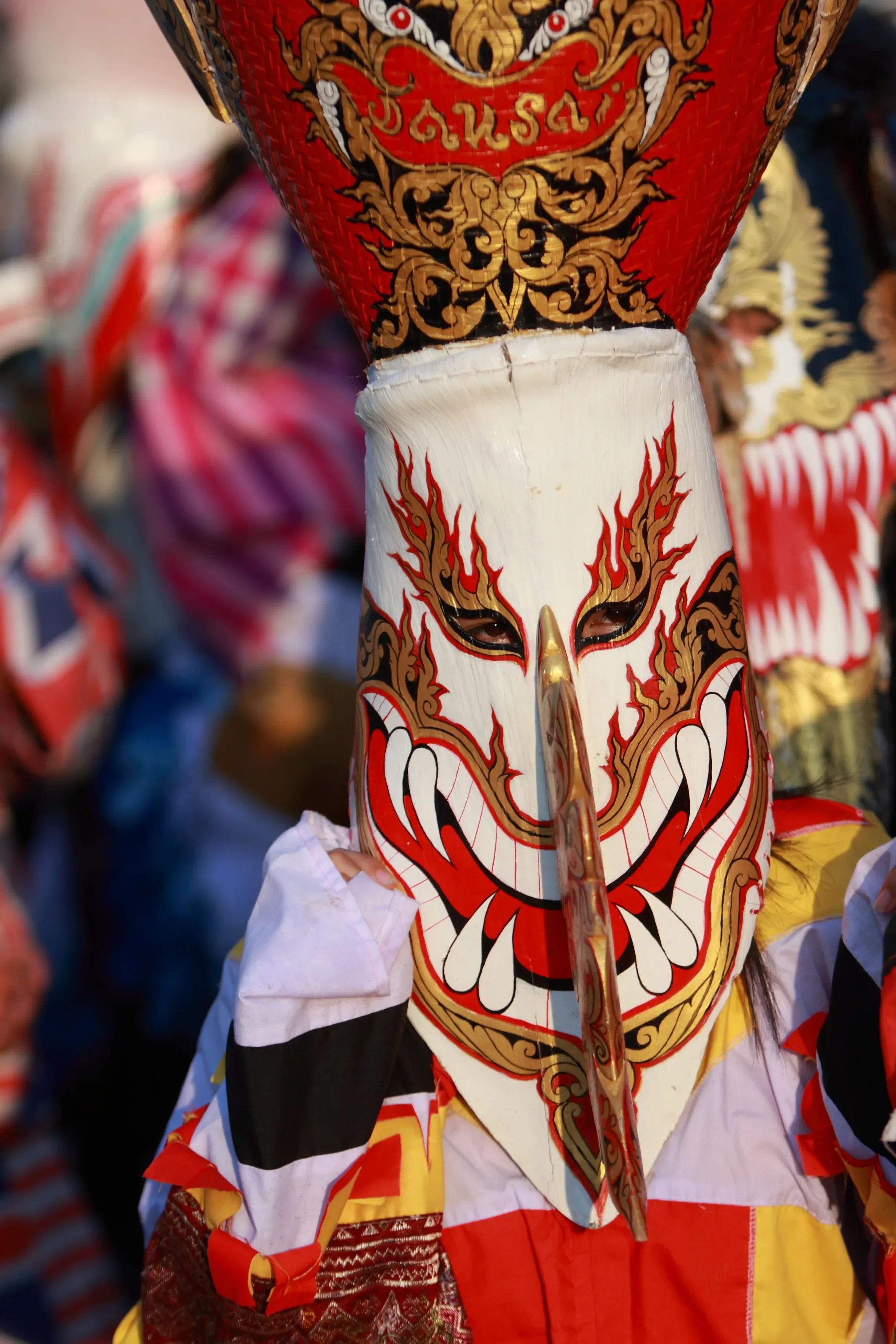 A Phi Ta Khon mask with festival crowds blurred behind it in Dan Sai