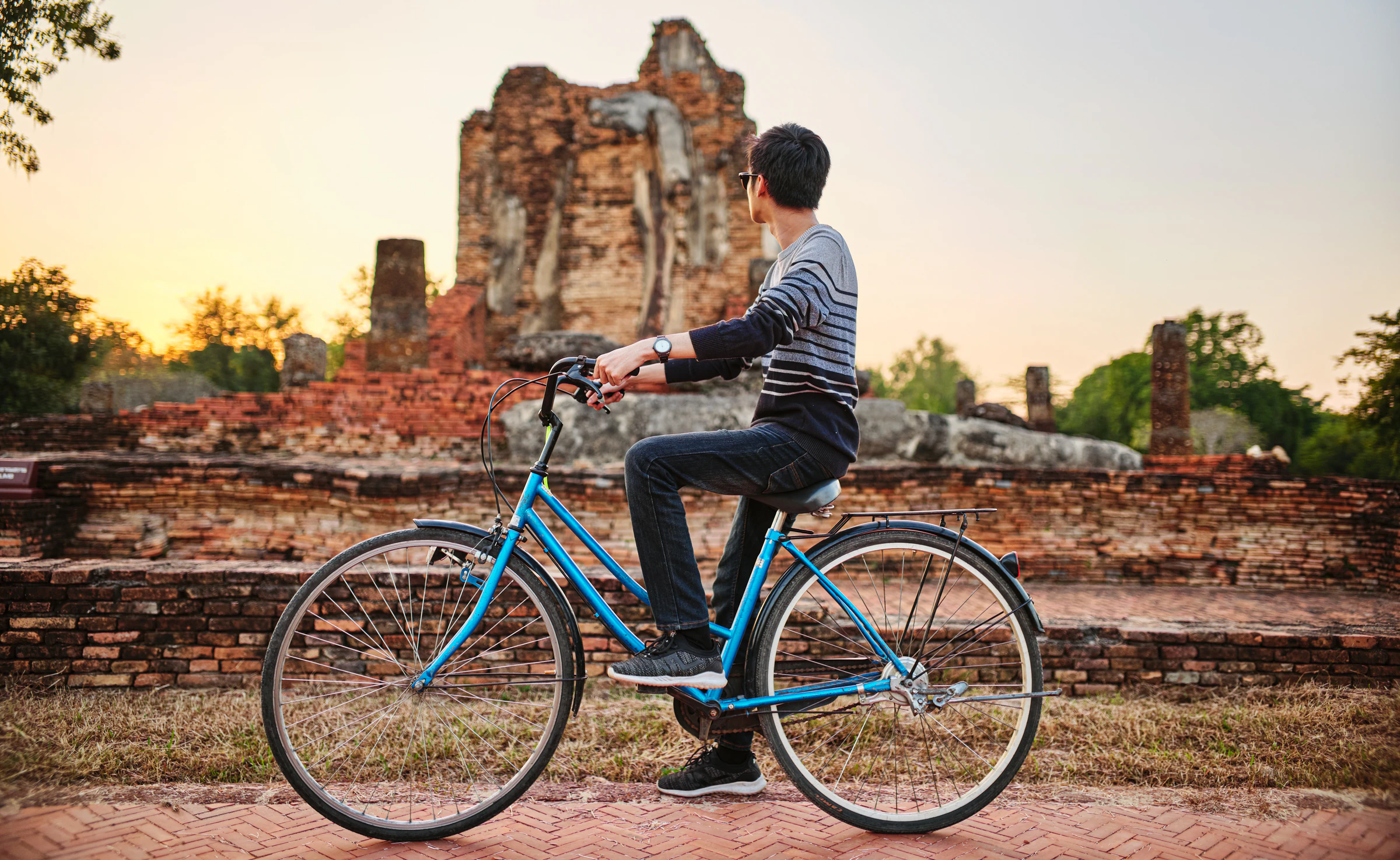 A visitor cycling past brick ruins at sunset in Sukhothai