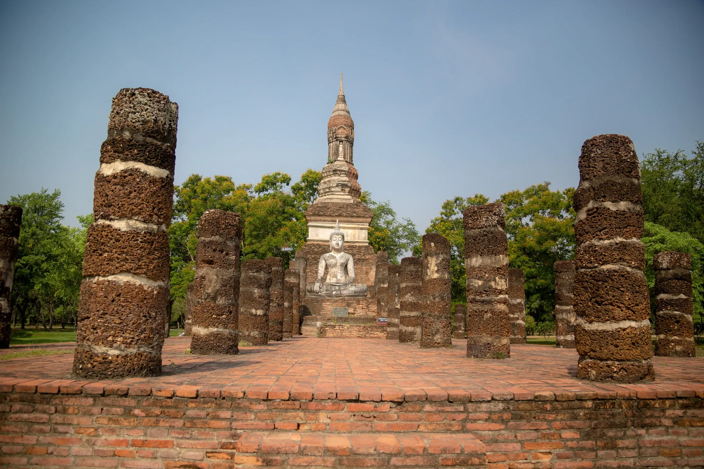 Laterite pillars and a seated Buddha among the ruins at Si Satchanalai Historical Park