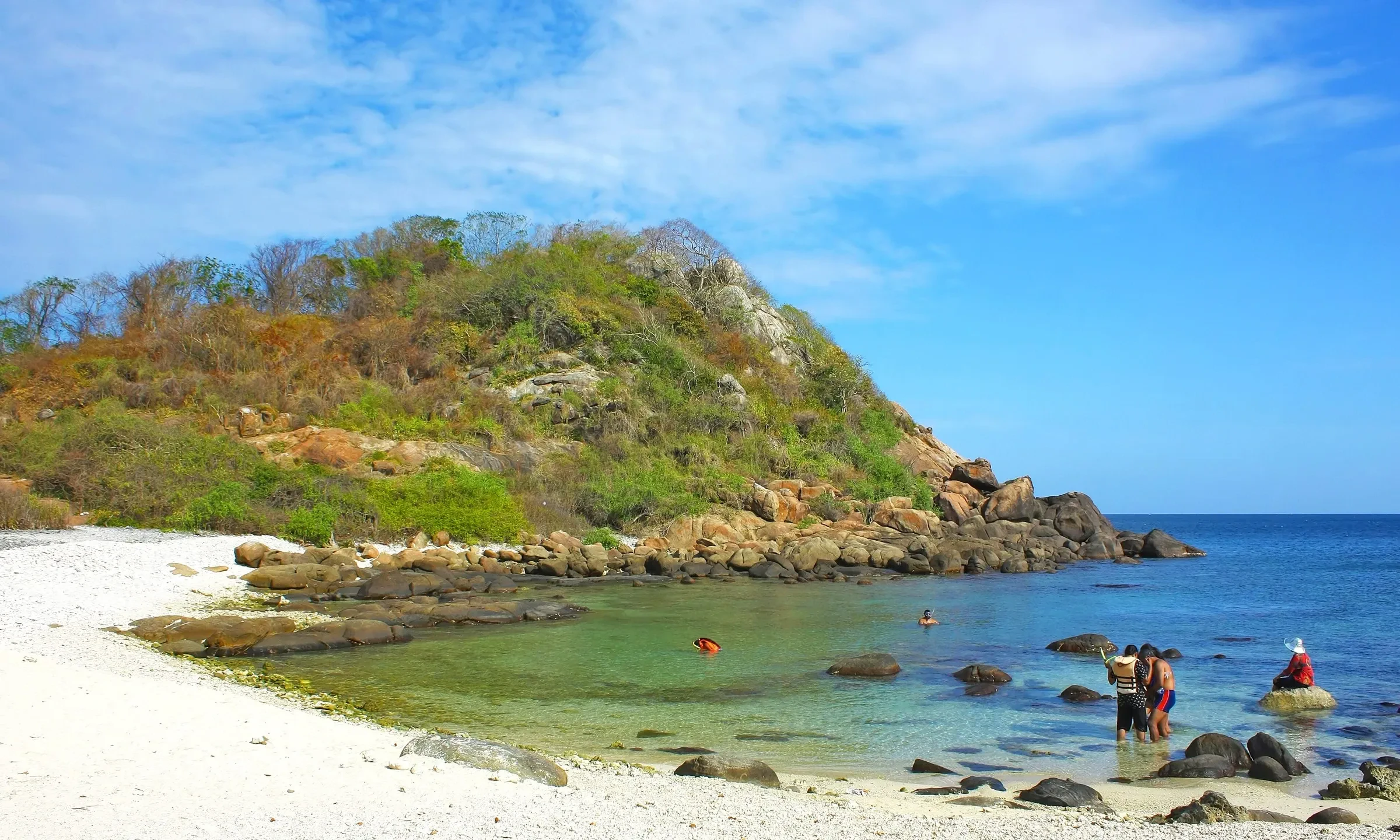 A small rocky headland and white sand beach on Pigeon Island National Park, with snorkellers wading in the shallows