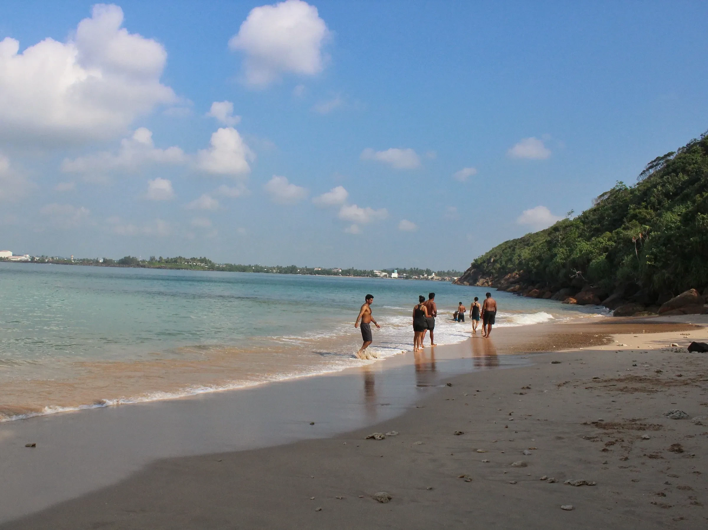 Visitors walking along the shoreline at Jungle Beach near Unawatuna, with the forested Rumassala headland beyond