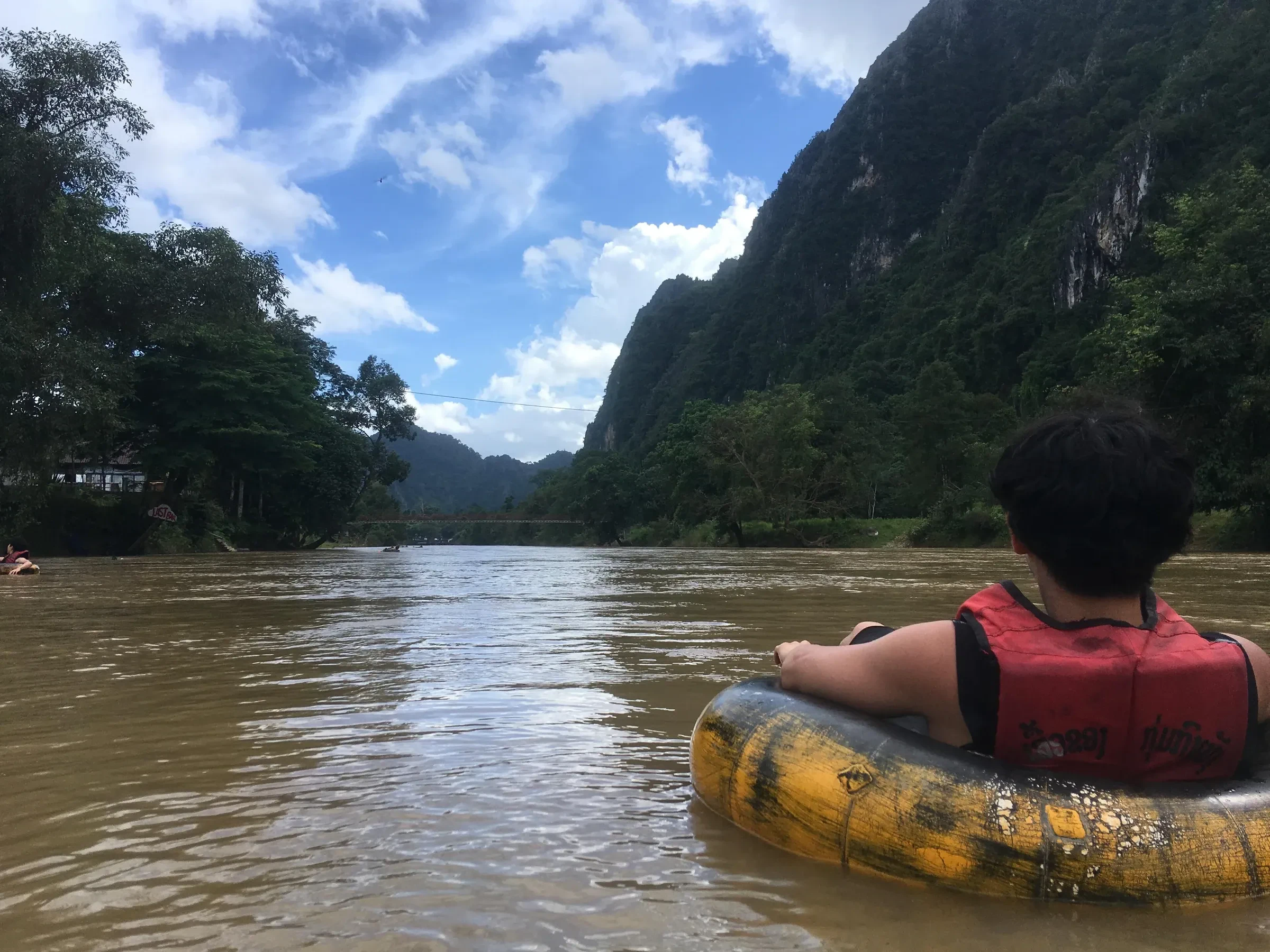 A traveller floating down the Nam Song in an inner tube, with karst cliffs behind