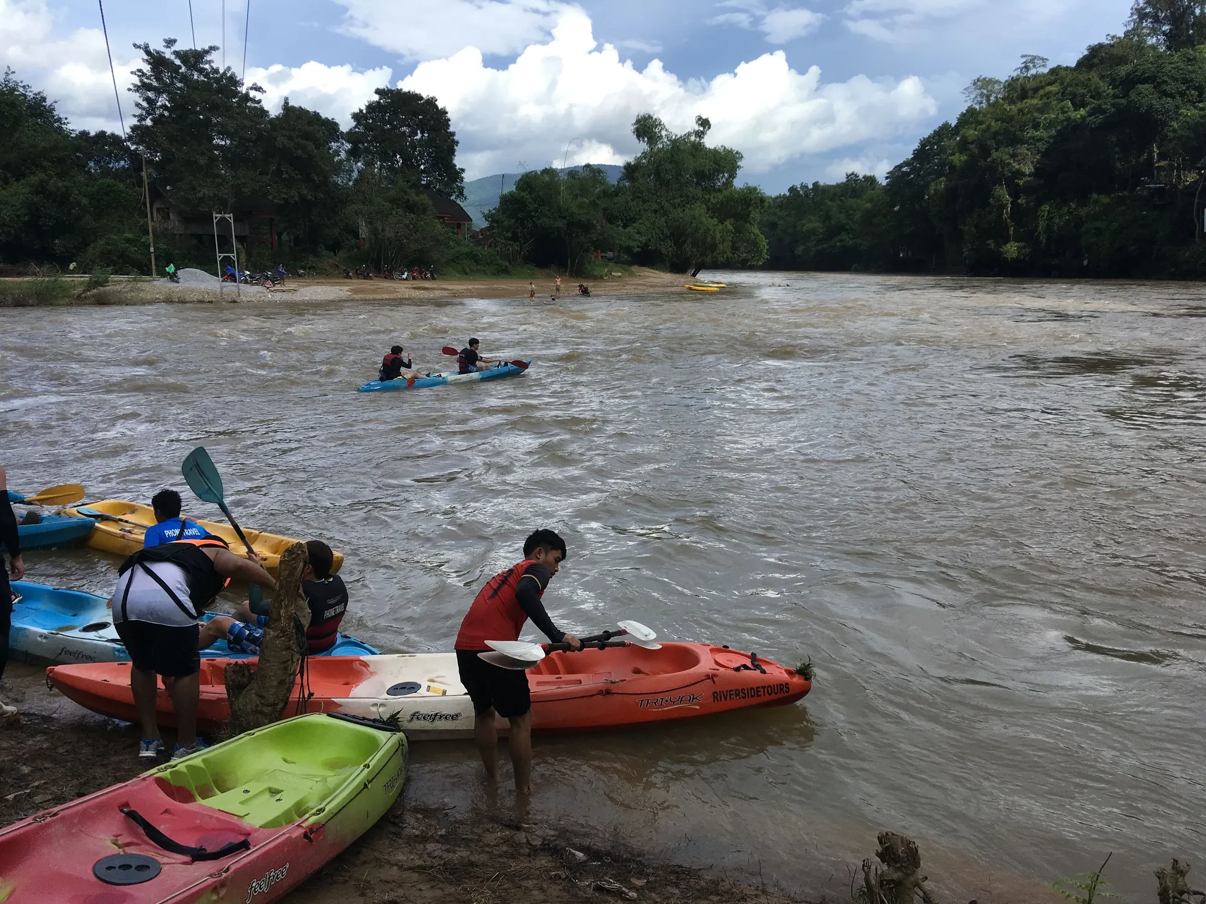 Kayakers on the Nam Song river at Vang Vieng, with forest along the far bank