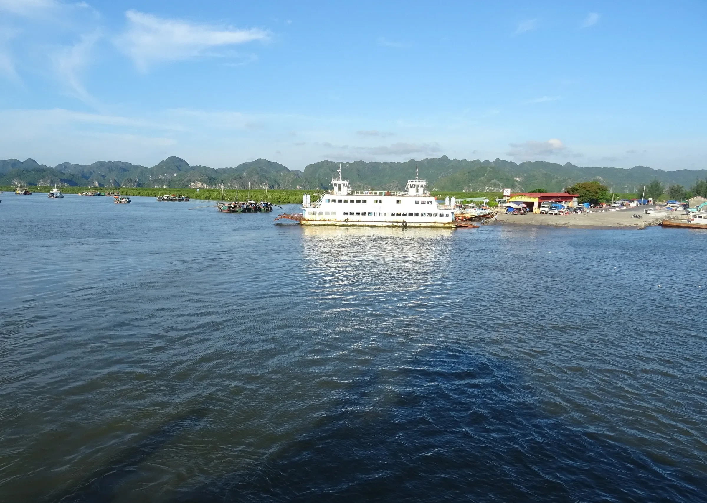A car ferry on calm water between Cat Ba and Cat Hai islands, green hills behind