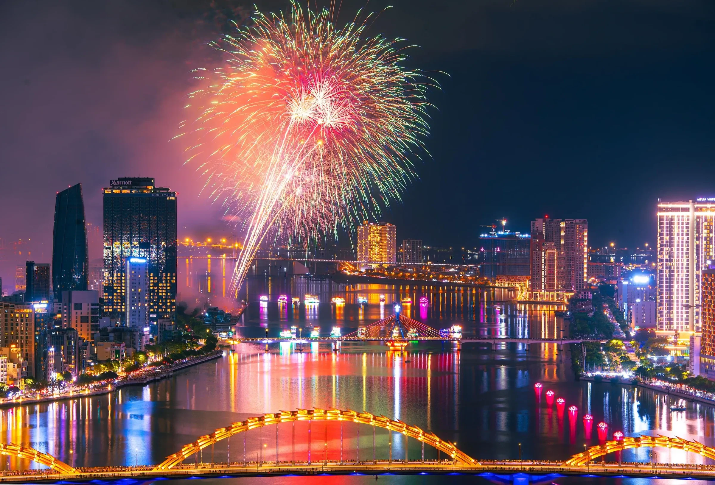 Aerial view of a firework burst over the Han River, with the Dragon Bridge and city lights below