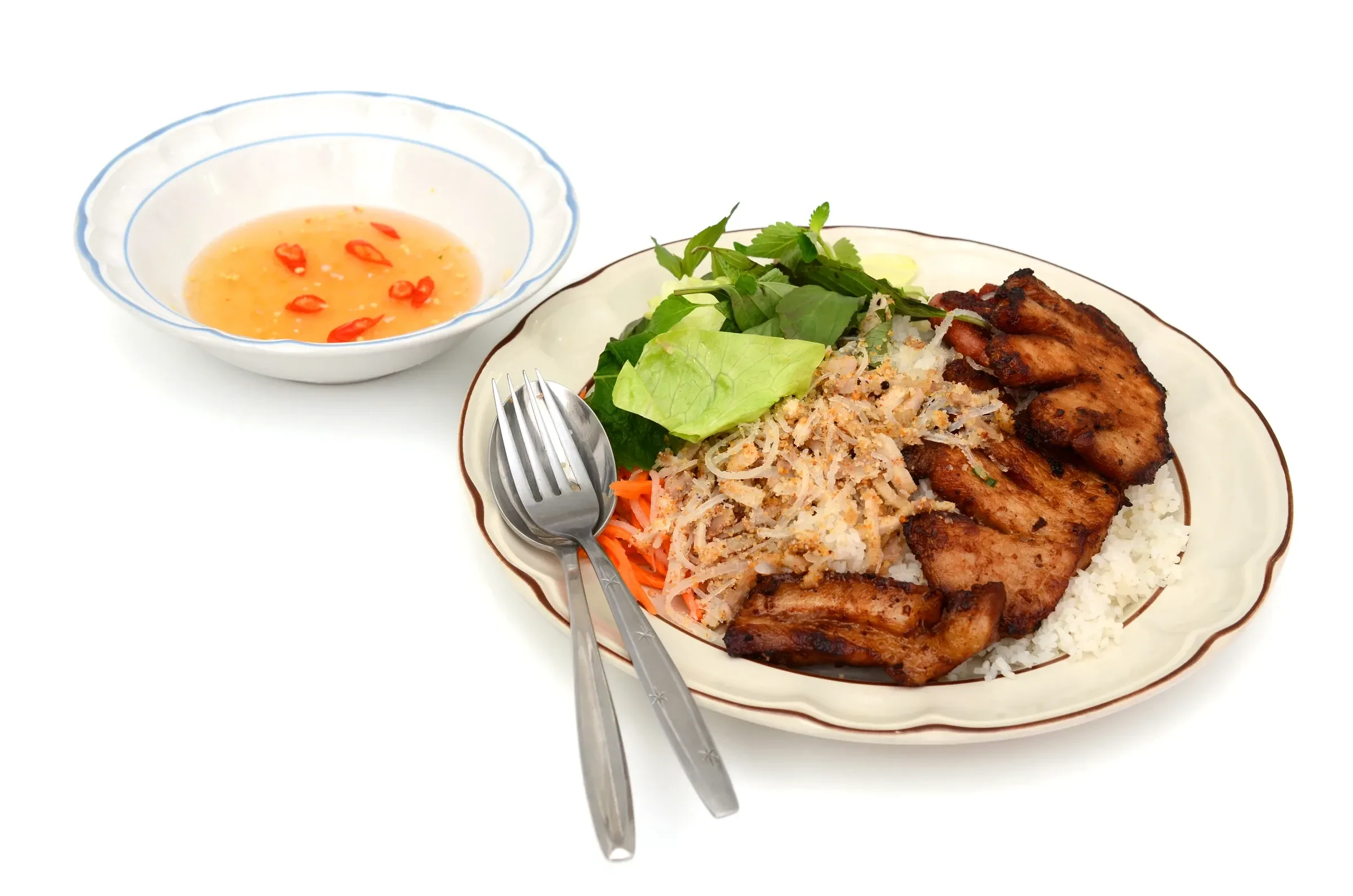 A plate of com tam broken rice with grilled pork, fresh vegetables and fish sauce