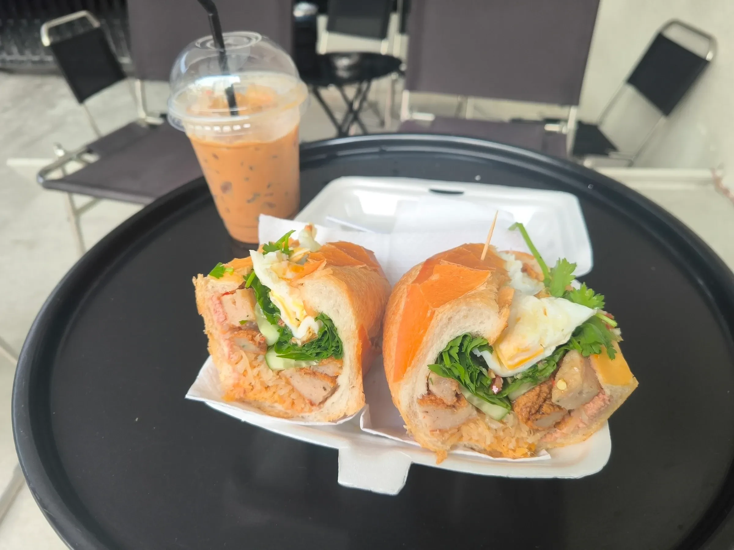 A halved banh mi with pork, egg and herbs beside an iced coffee in Ho Chi Minh City