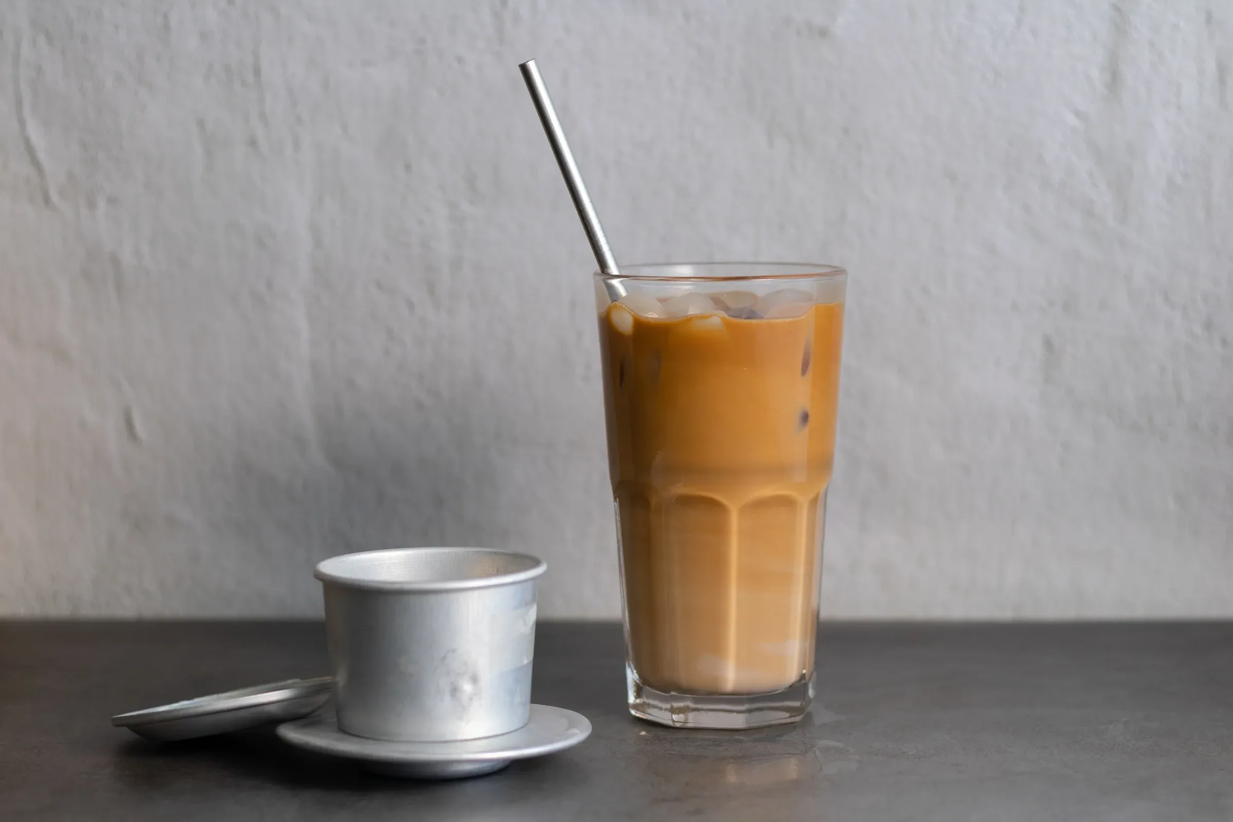 A glass of Vietnamese iced coffee with a phin filter behind it