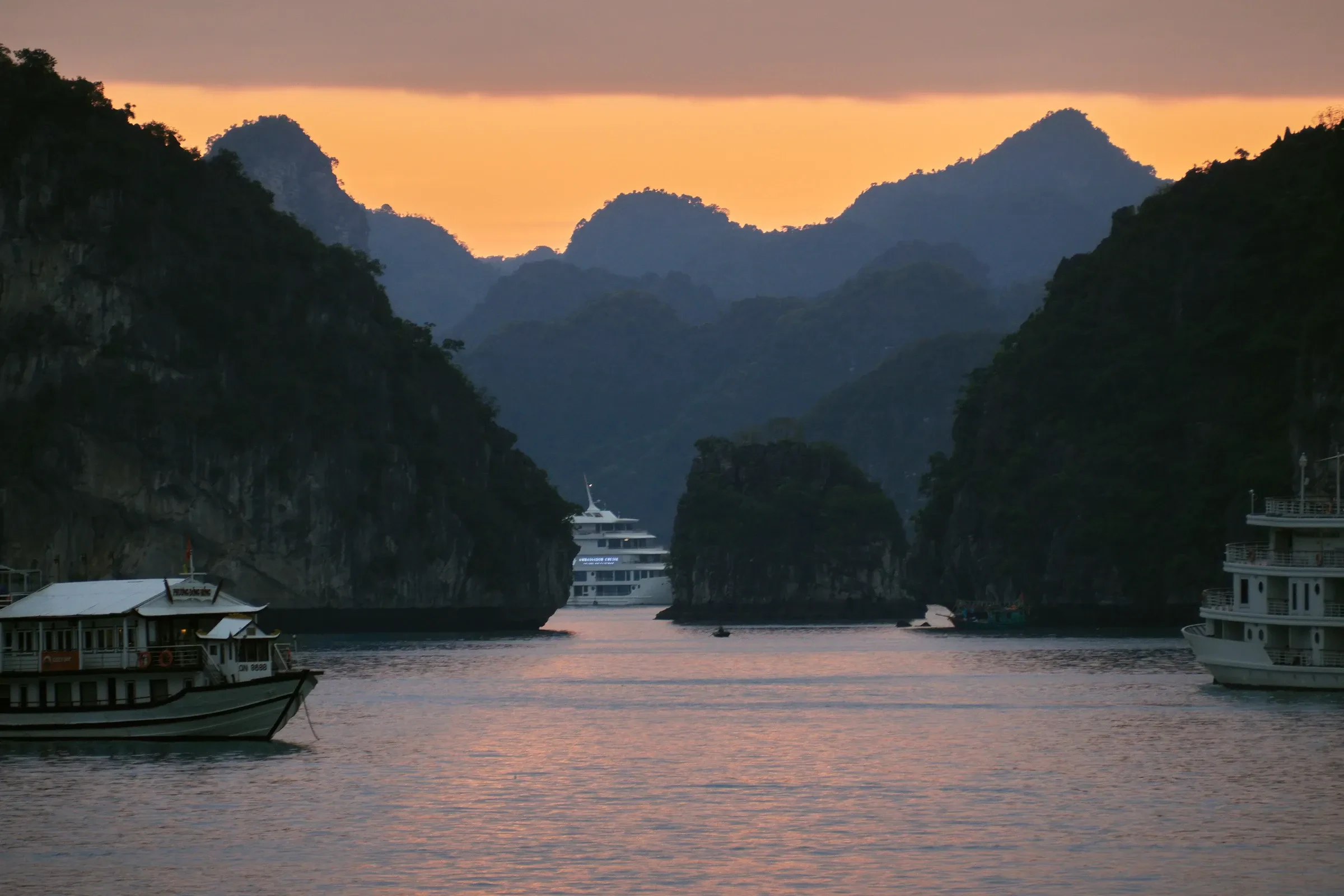 Cruise and tour boats anchored among limestone islands in Ha Long Bay at dusk