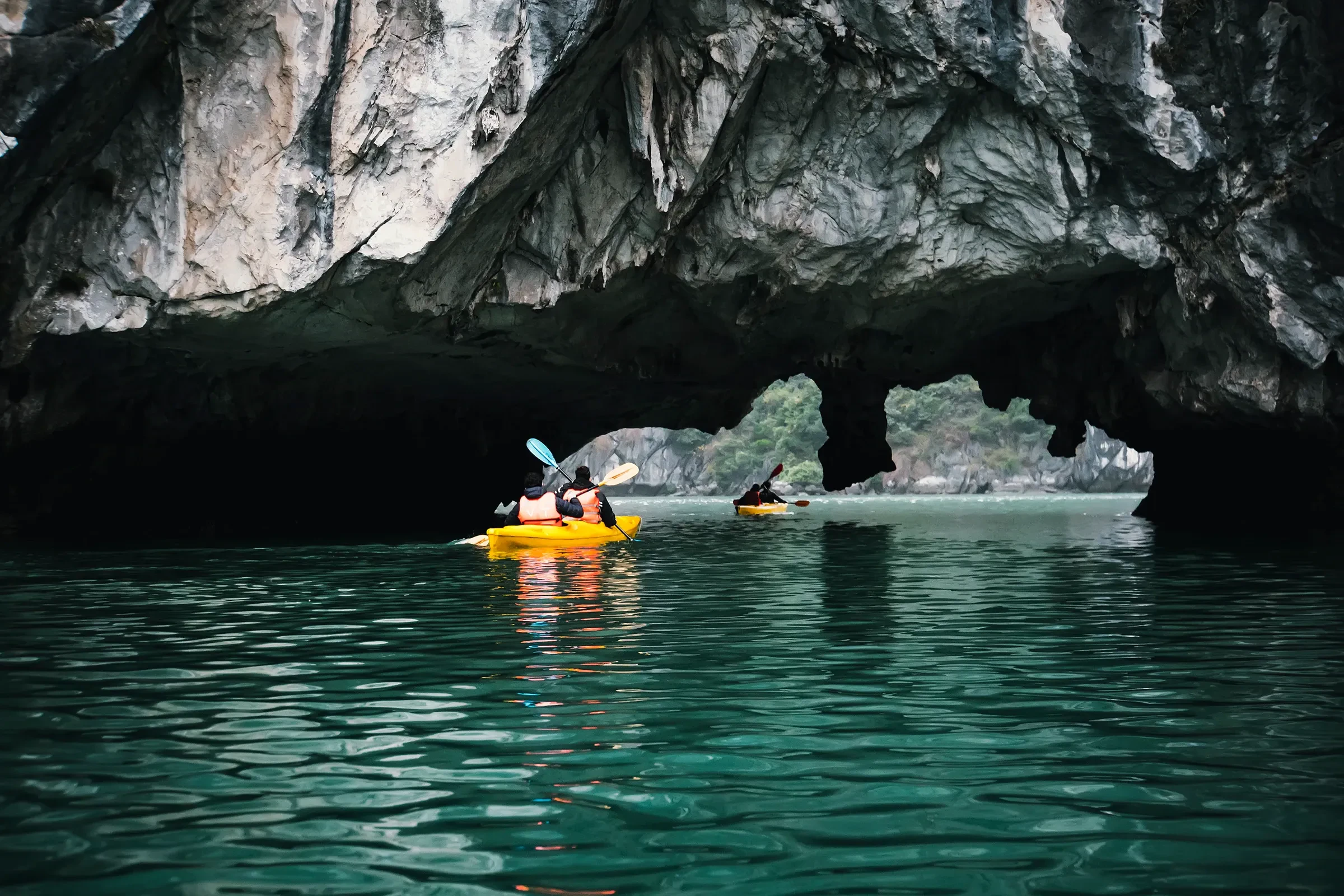 Two kayakers paddling toward a limestone cave arch near Cat Ba Island in Ha Long Bay