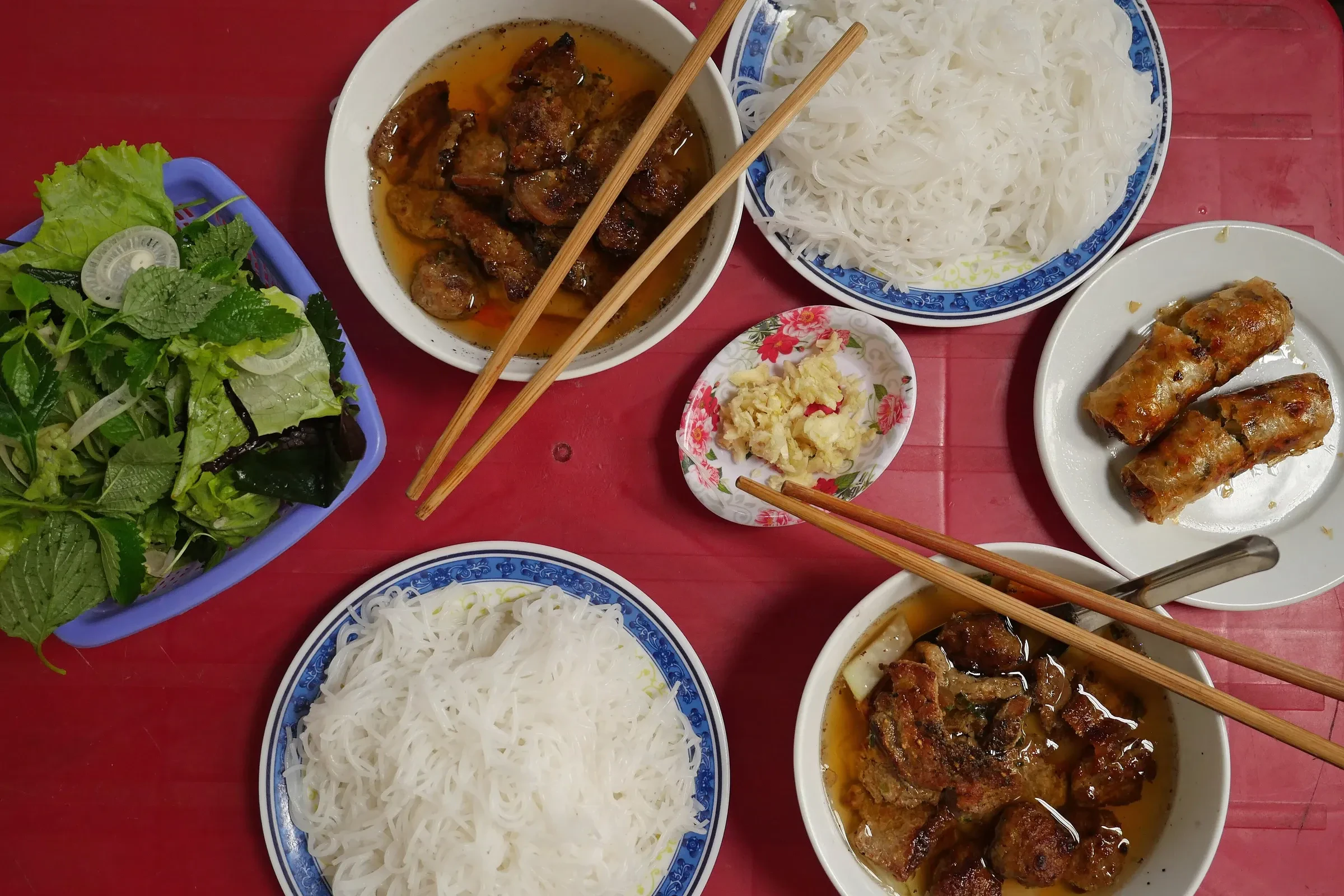 A table set for bun cha in Hanoi, with grilled pork in broth, rice noodles, herbs and fried spring rolls