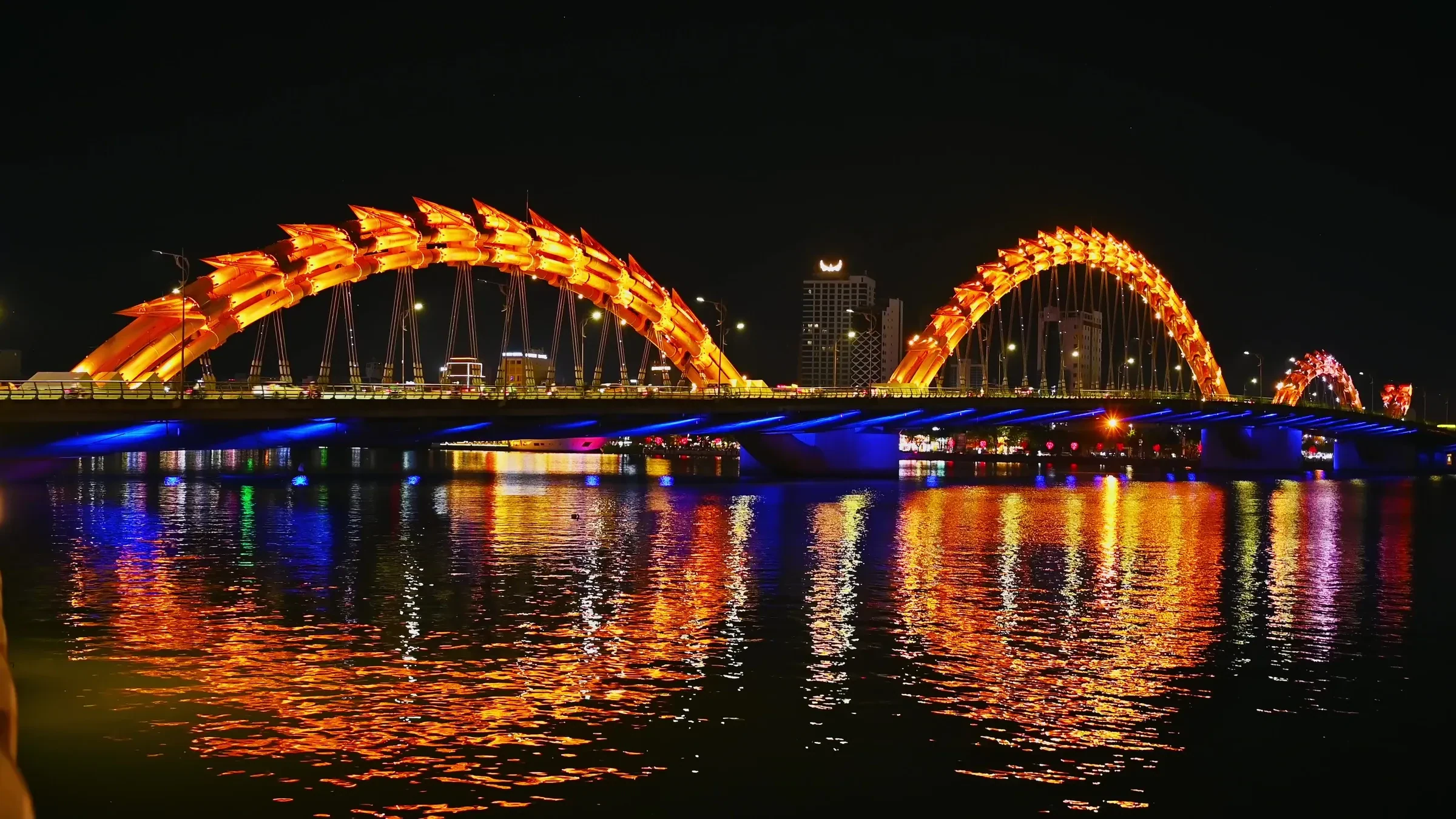 The Dragon Bridge in Da Nang lit orange and blue over the Han River at night