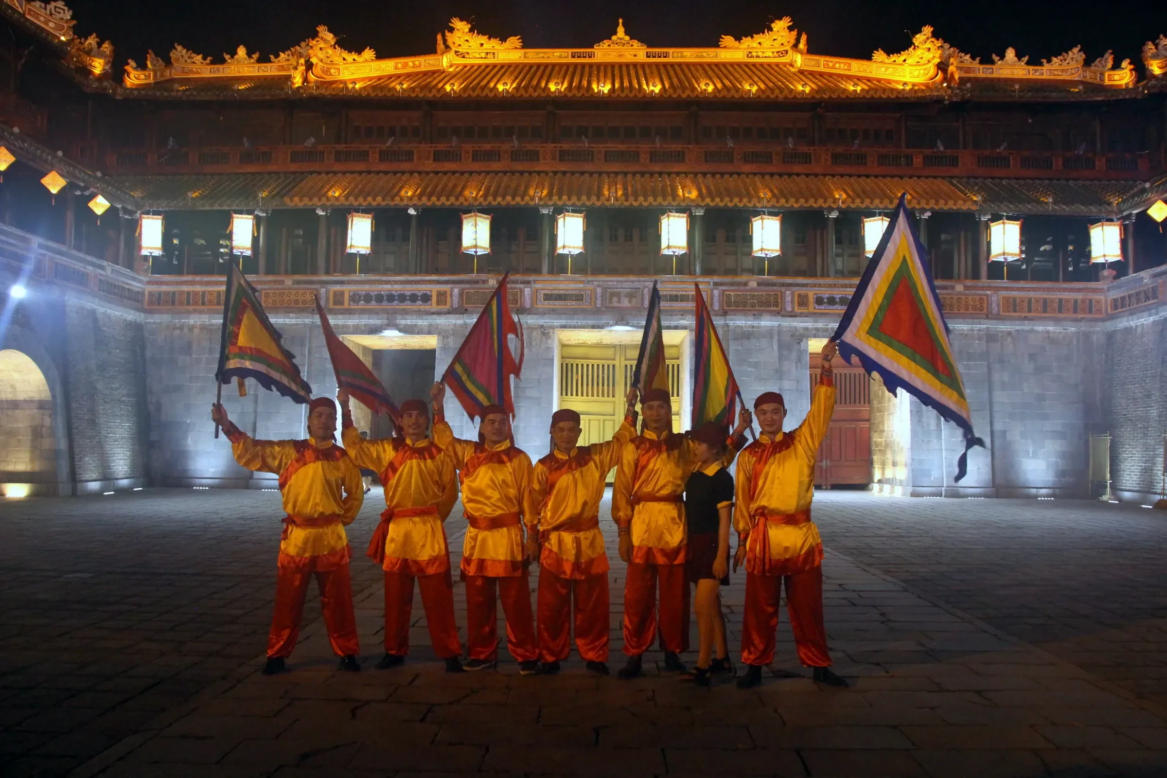 Flag bearers in royal costume in front of Ngo Mon Gate at Hue's Imperial City, lit at night during a Hue Festival performance