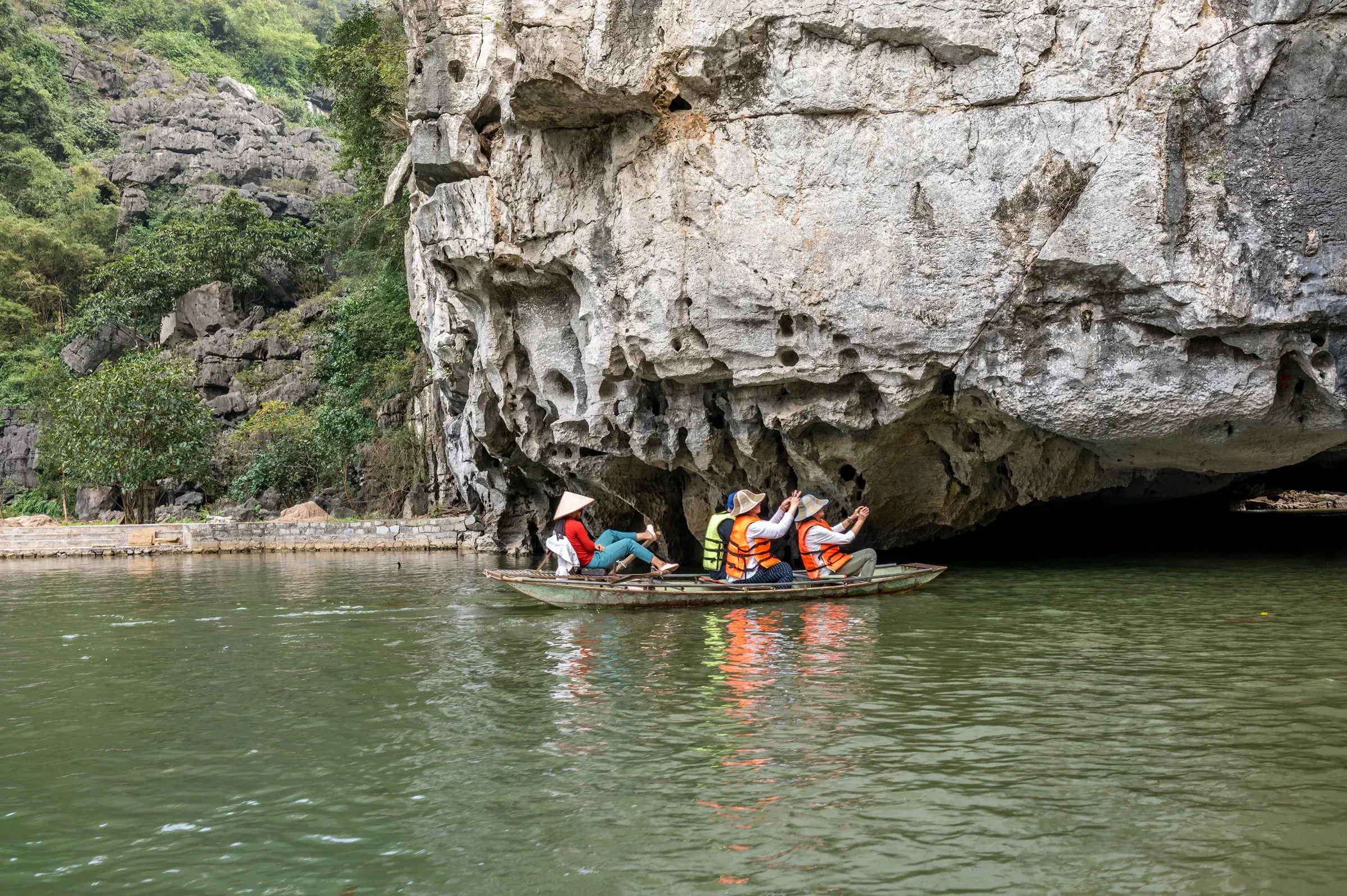 A rowing boat of visitors leaving a limestone cave on the Ngo Dong River at Tam Coc, Ninh Binh