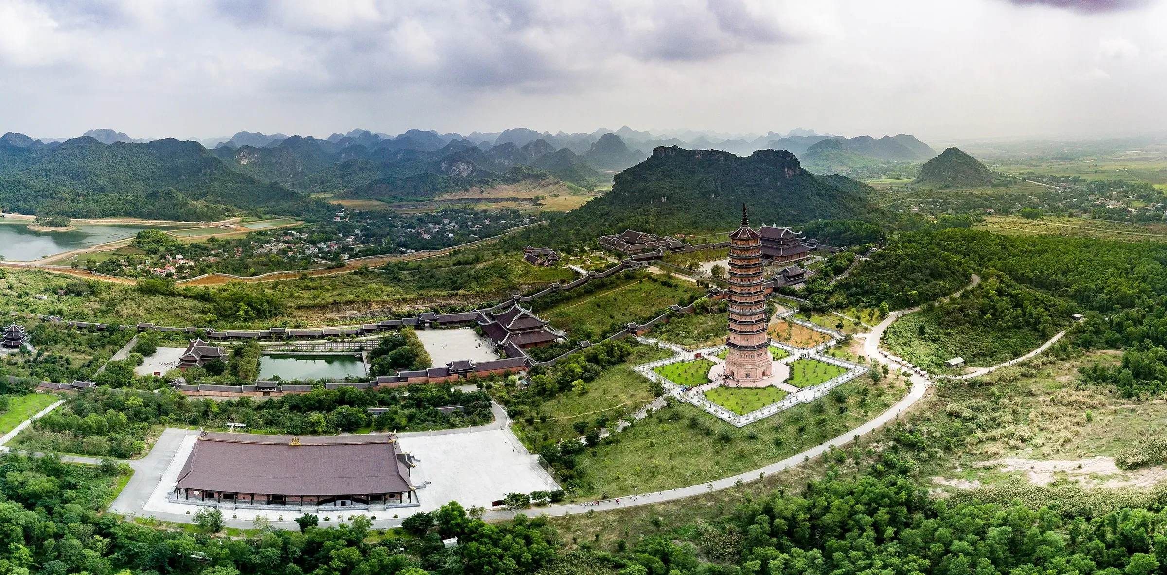 An aerial view of the tall pagoda and temple halls at Bai Dinh, set among green karst hills in Ninh Binh