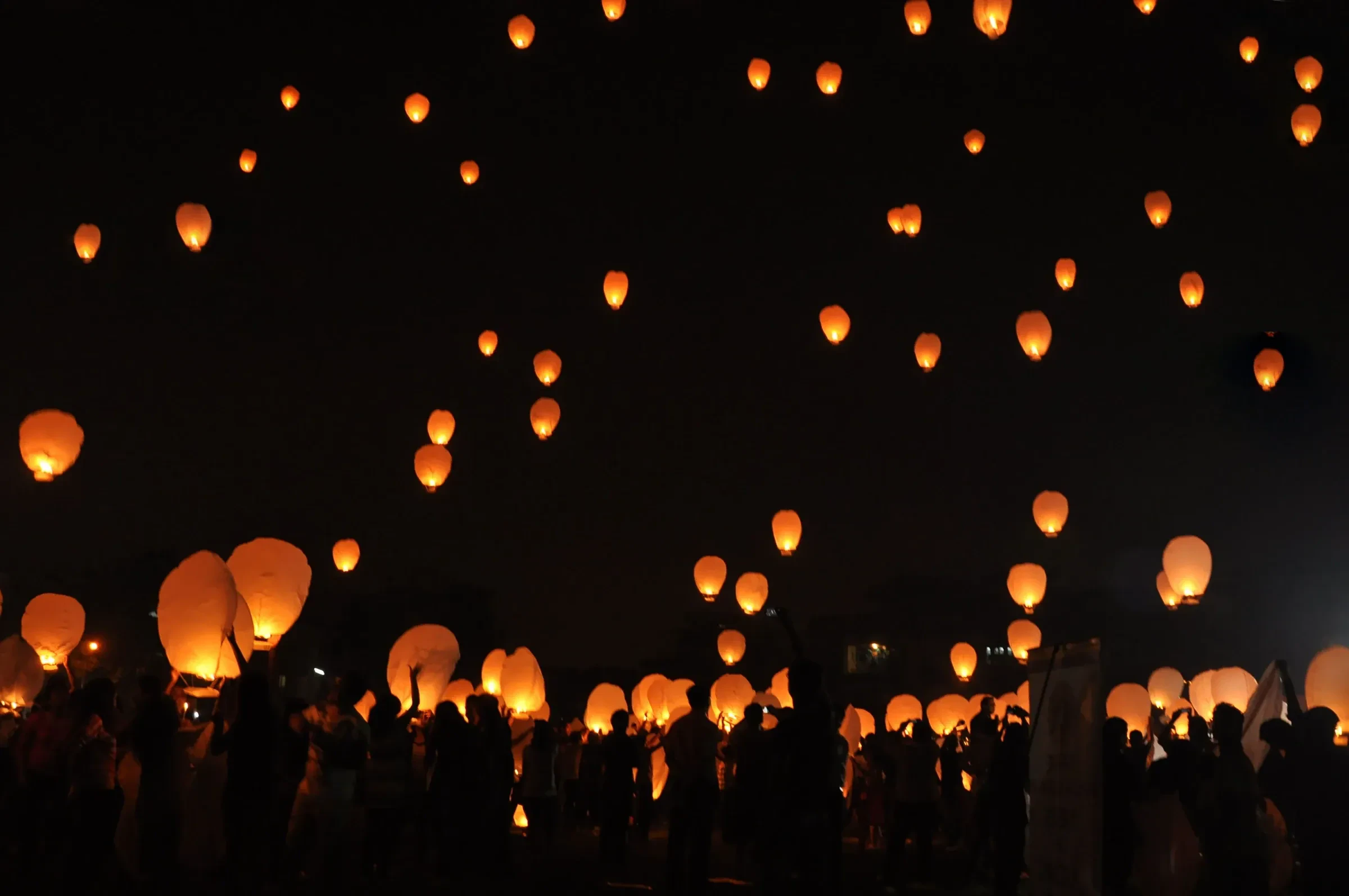 Hundreds of sky lanterns rising above a crowd at night