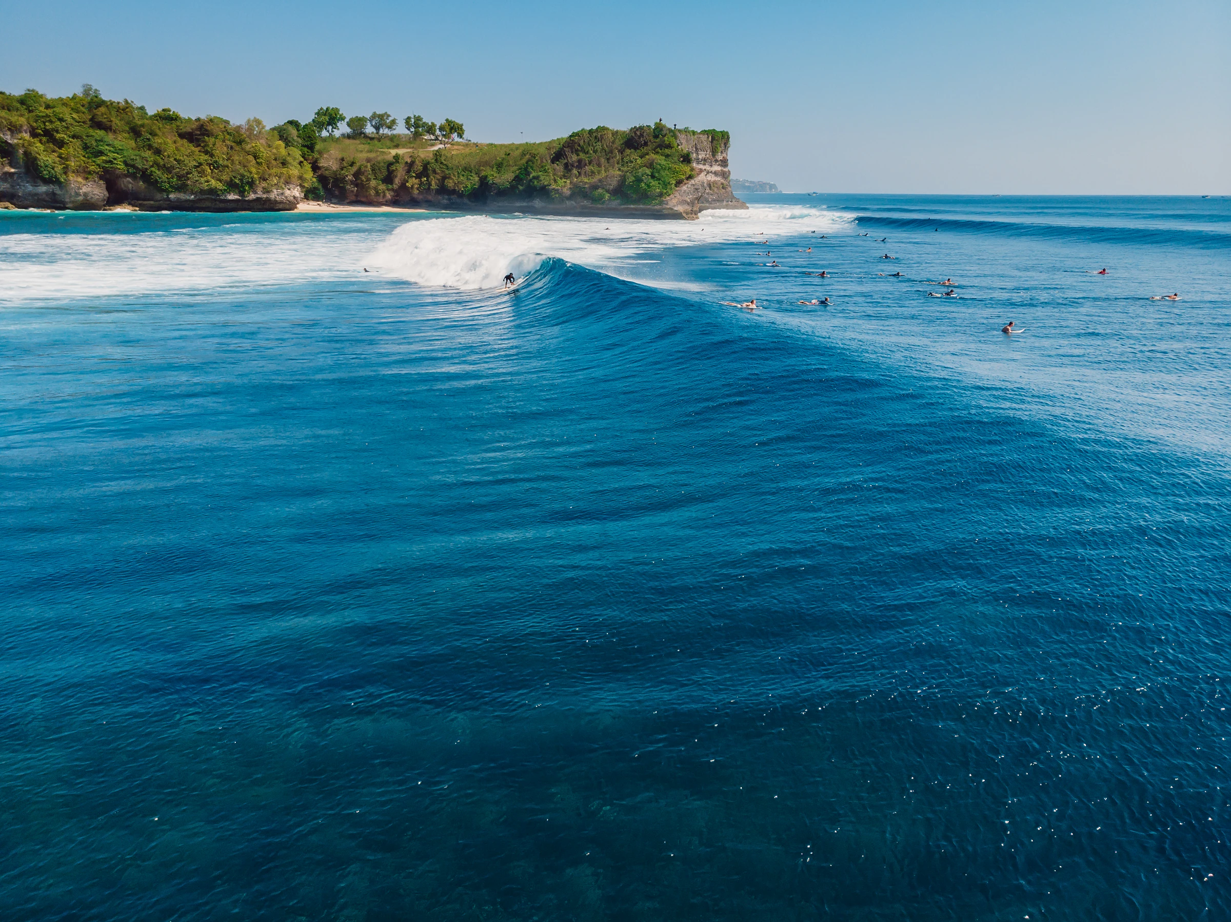 Aerial view of surfers riding a large wave near a cliff at Uluwatu, Bali
