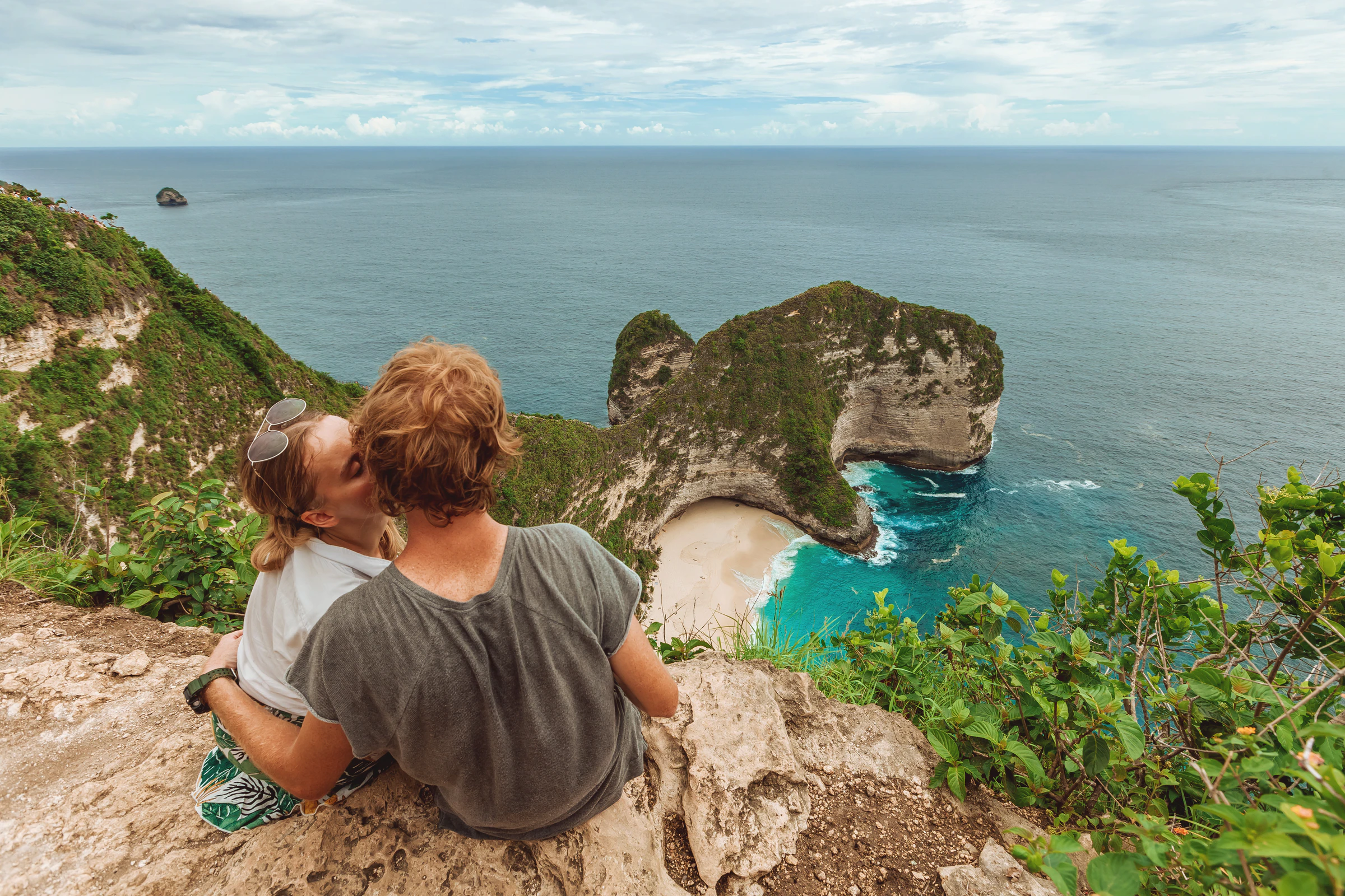 A couple sitting close together looking out over Kelingking Beach on Nusa Penida, Indonesia