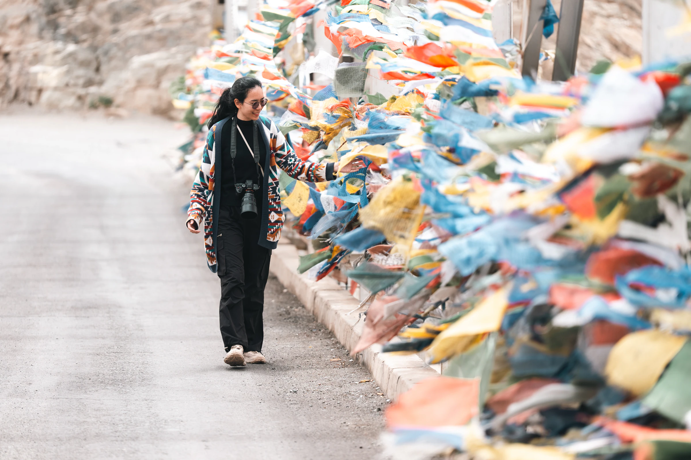A woman with a camera walking past strings of Tibetan prayer flags in Ladakh, India