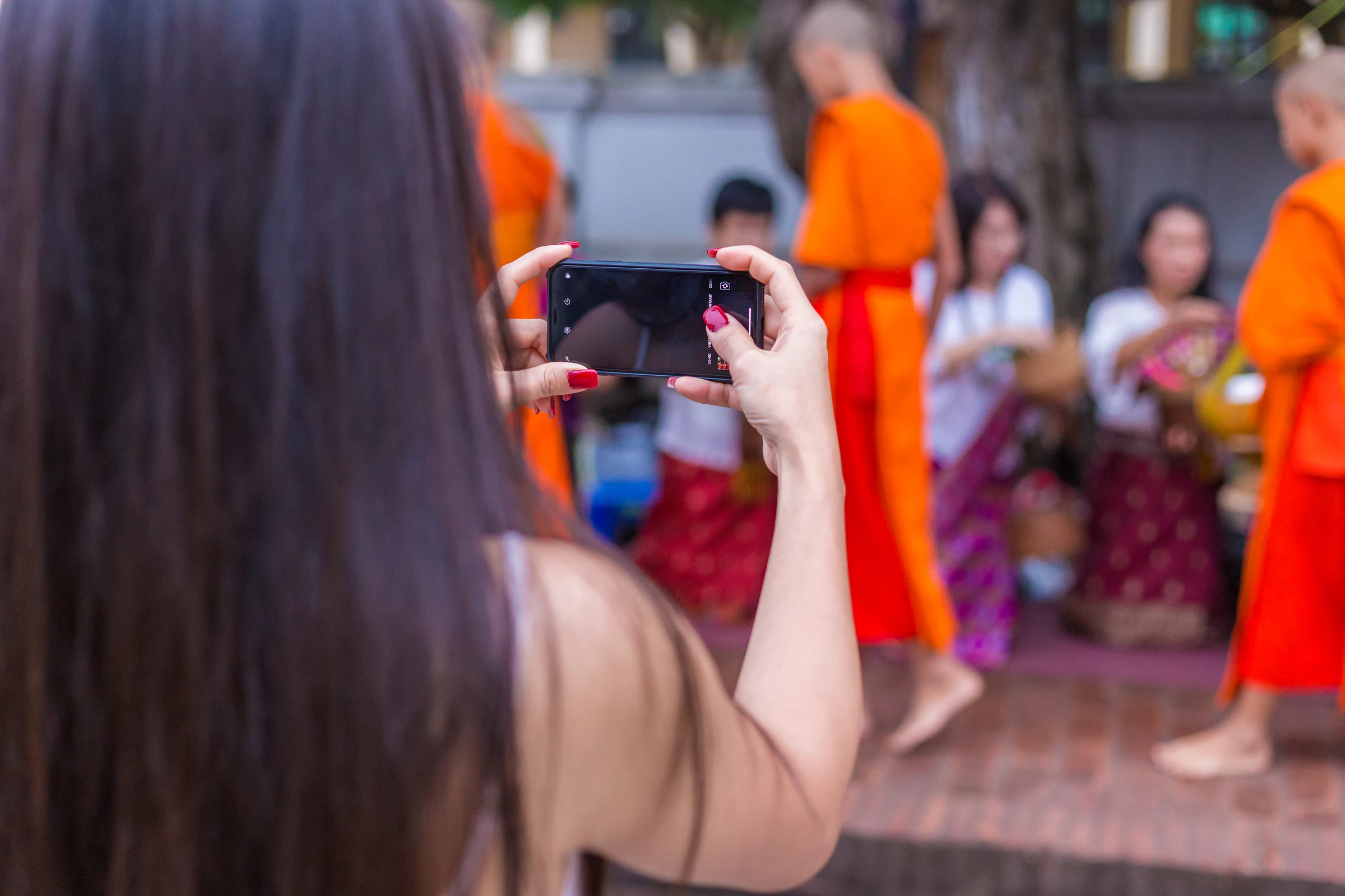 A tourist photographing monks collecting morning alms from local people in Luang Prabang, Laos