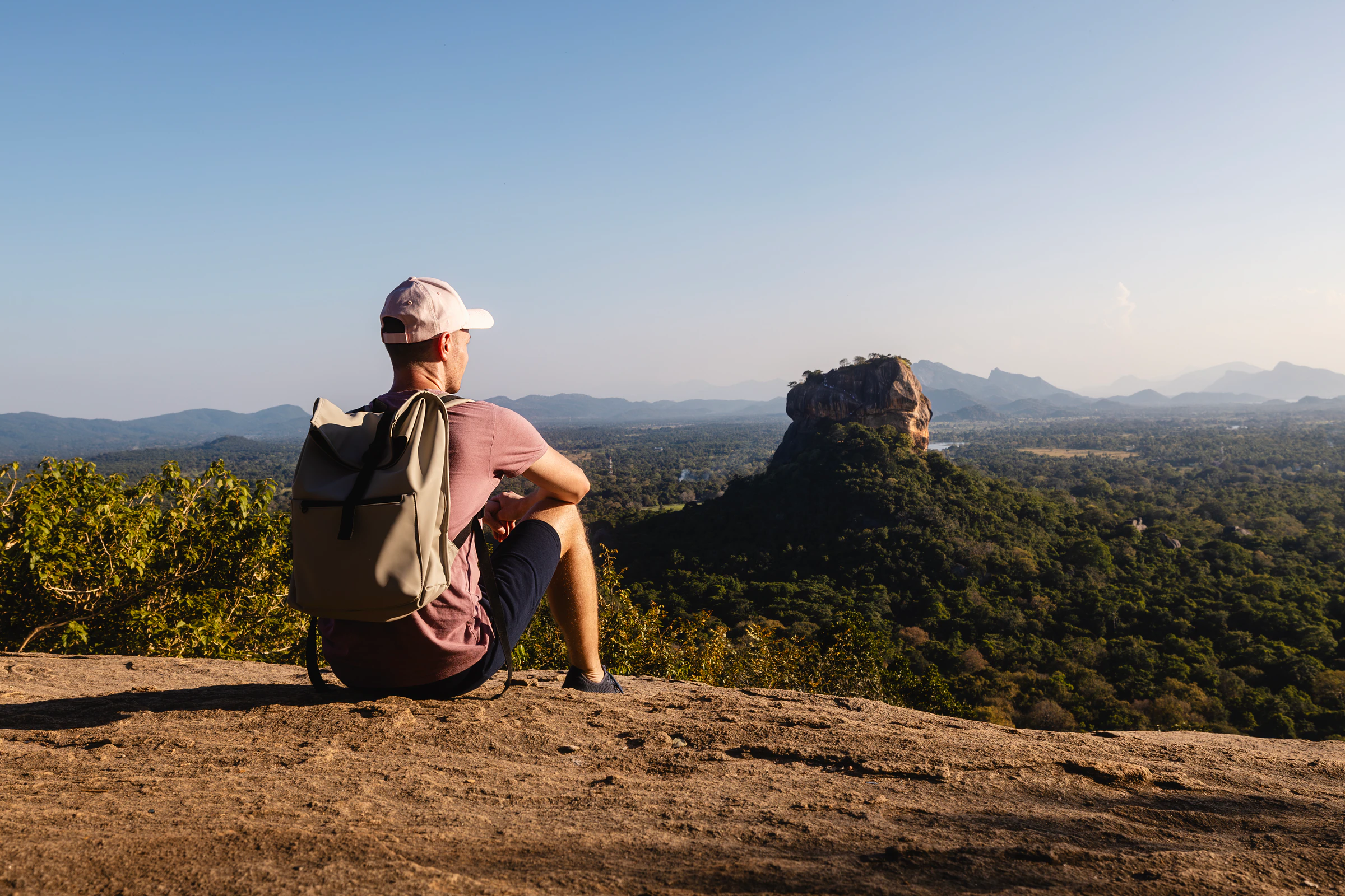 A traveller sitting on a rock looking out at Sigiriya rock in the distance, Sri Lanka