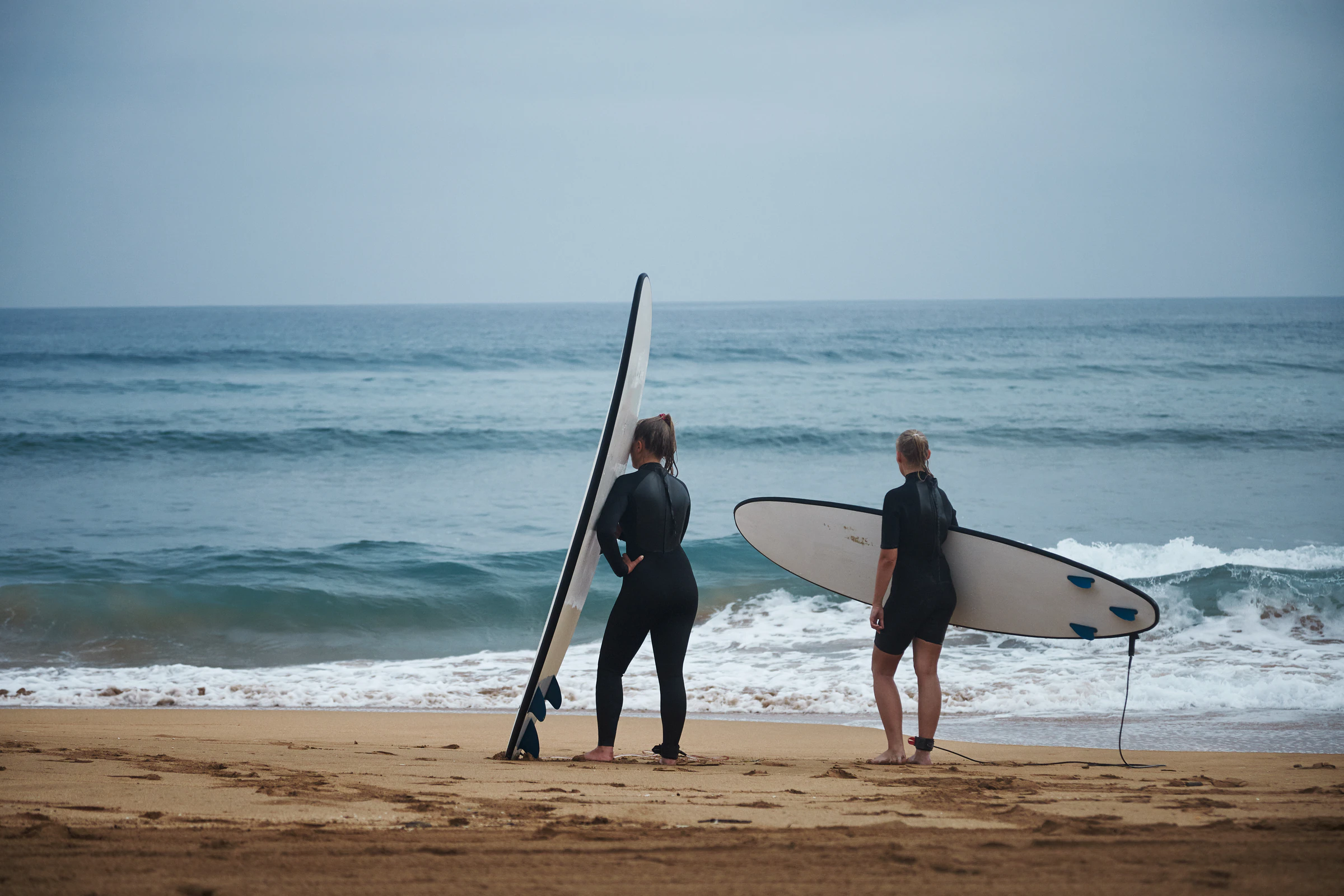 Two women carrying surfboards down to the water on a beach in Sri Lanka