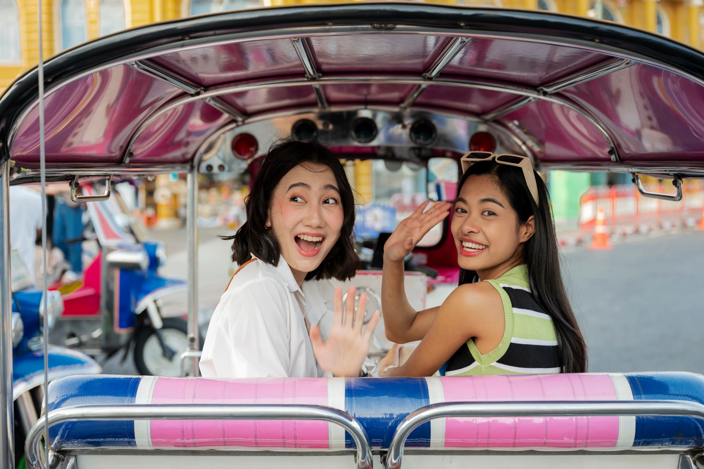 Two women waving from the back of a tuk-tuk in Bangkok, Thailand
