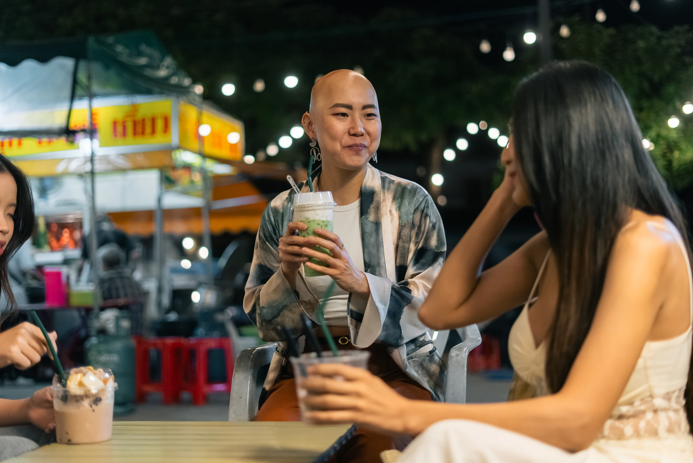 Friends sitting with drinks at a night market food stall in Bangkok, Thailand