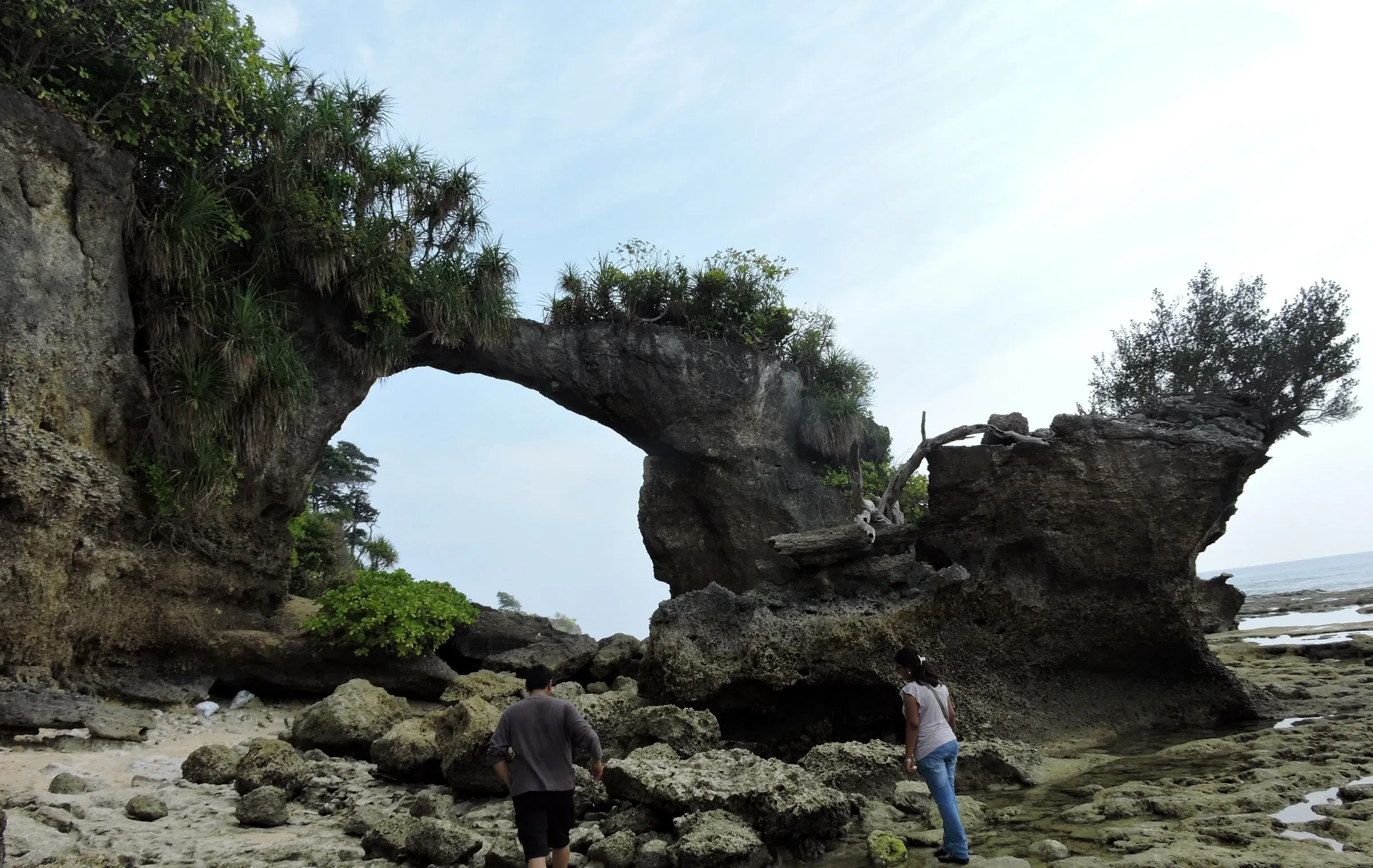 The Natural Bridge, a rock arch on the shore of Neil Island, with two people beside it