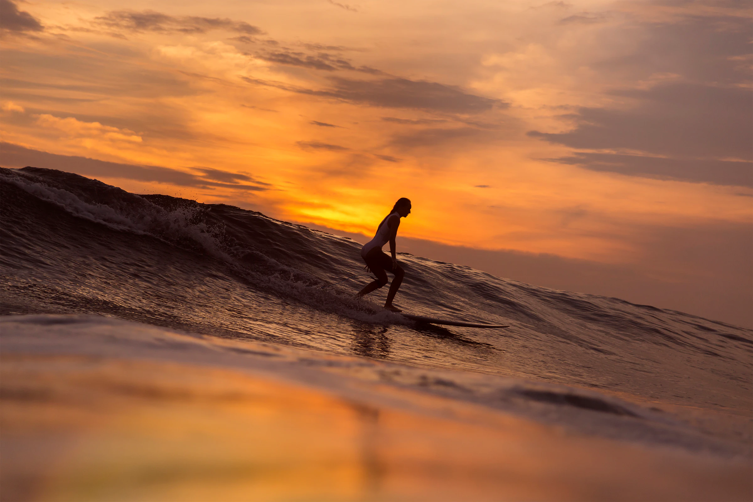A surfer riding a wave under a golden sunset sky