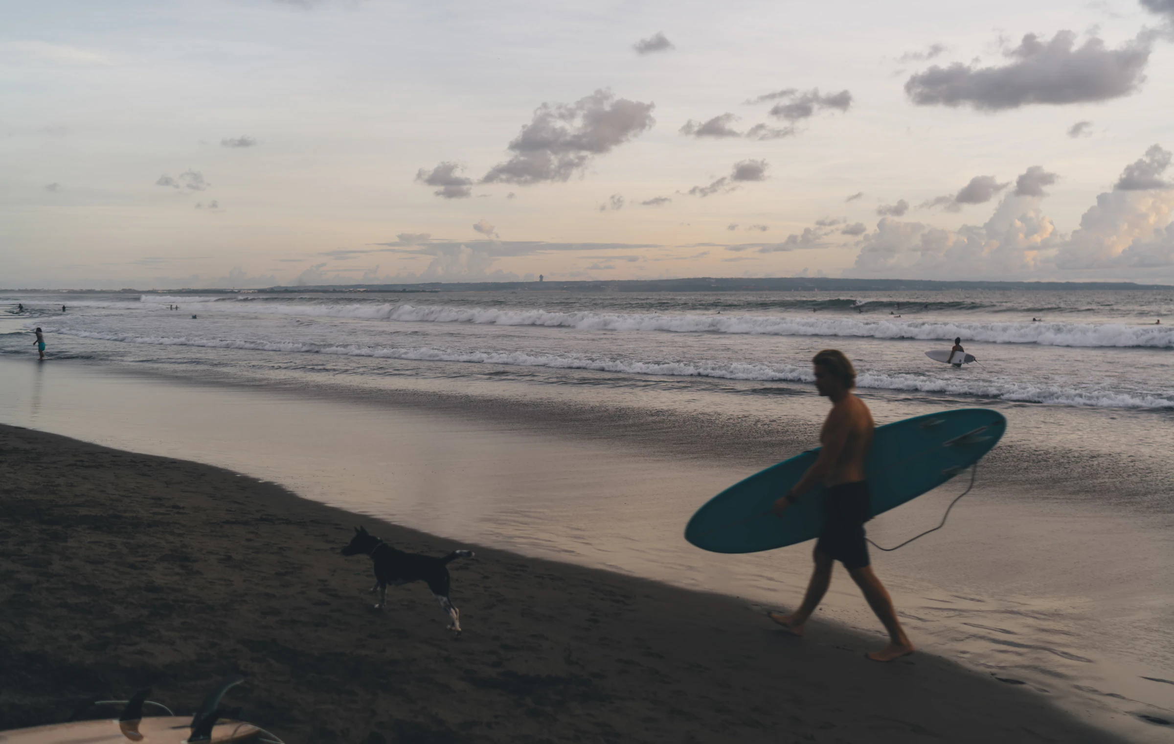 A surfer carrying a board along the beach at dusk